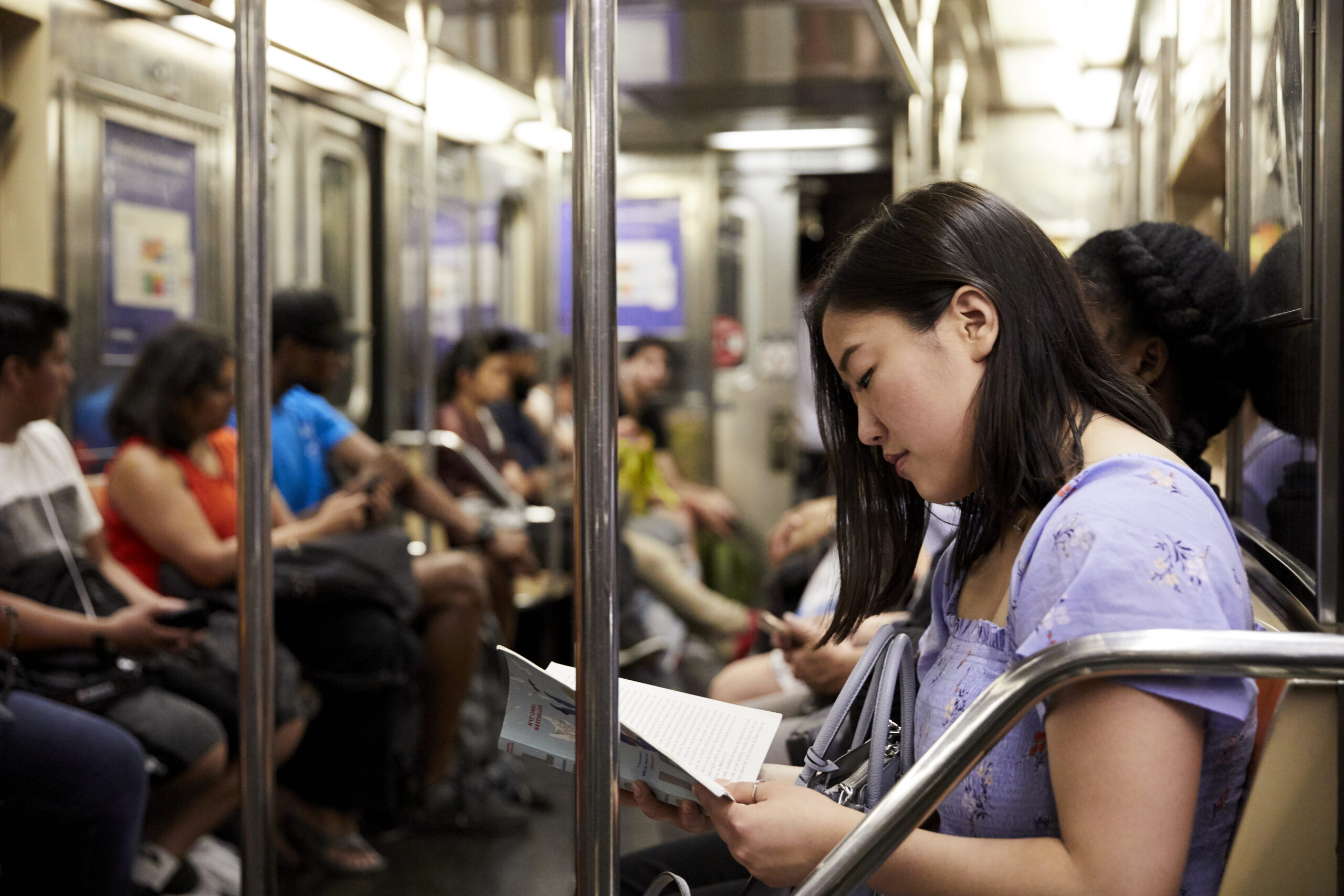 A student reading a book on a busy NYC subway car filled with fellow passengers.