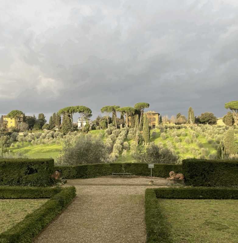 Manicured, green gardens are in front of a landscape of trees and hills.