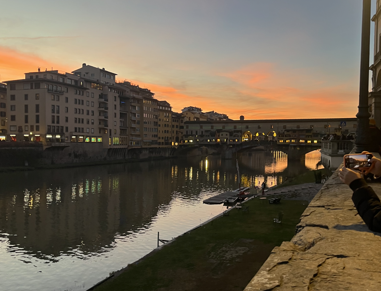 The Arno River surrounded by old buildings with the sky a gradient of blue to orange as the sun sets.