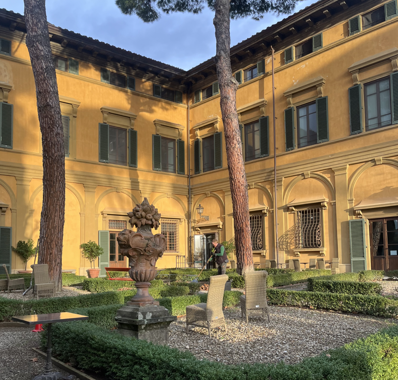An outdoor courtyard with a fountain in the center, surrounded by the yellow walls of a Renaissance villa