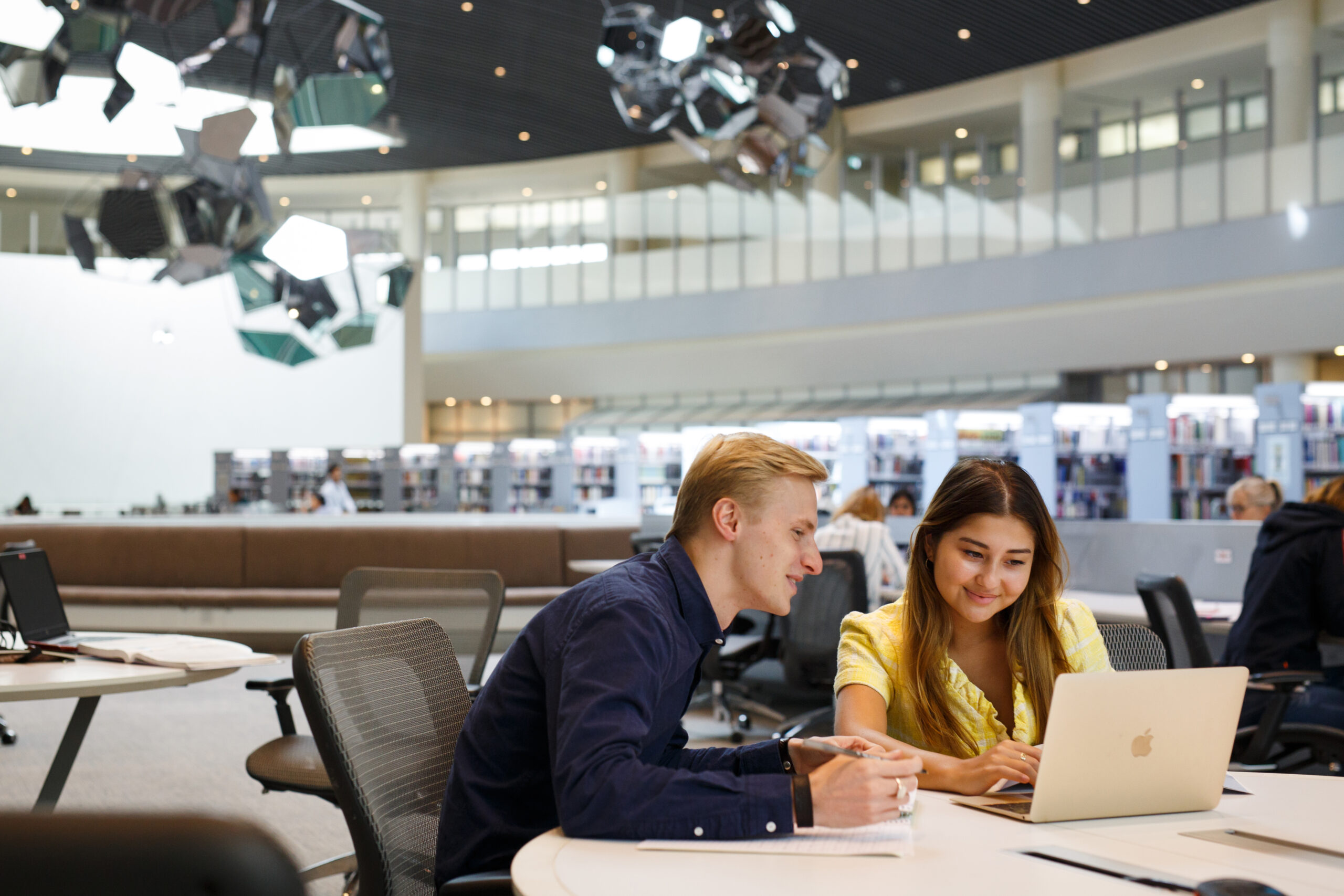 Two students sit together at a table in the NYU Abu Dhabi library, studying side by side.