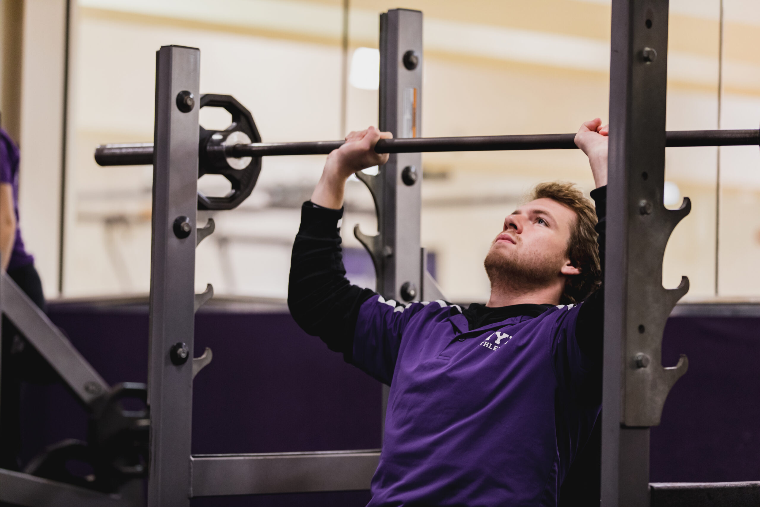 A student lifts a barbell in the gym.