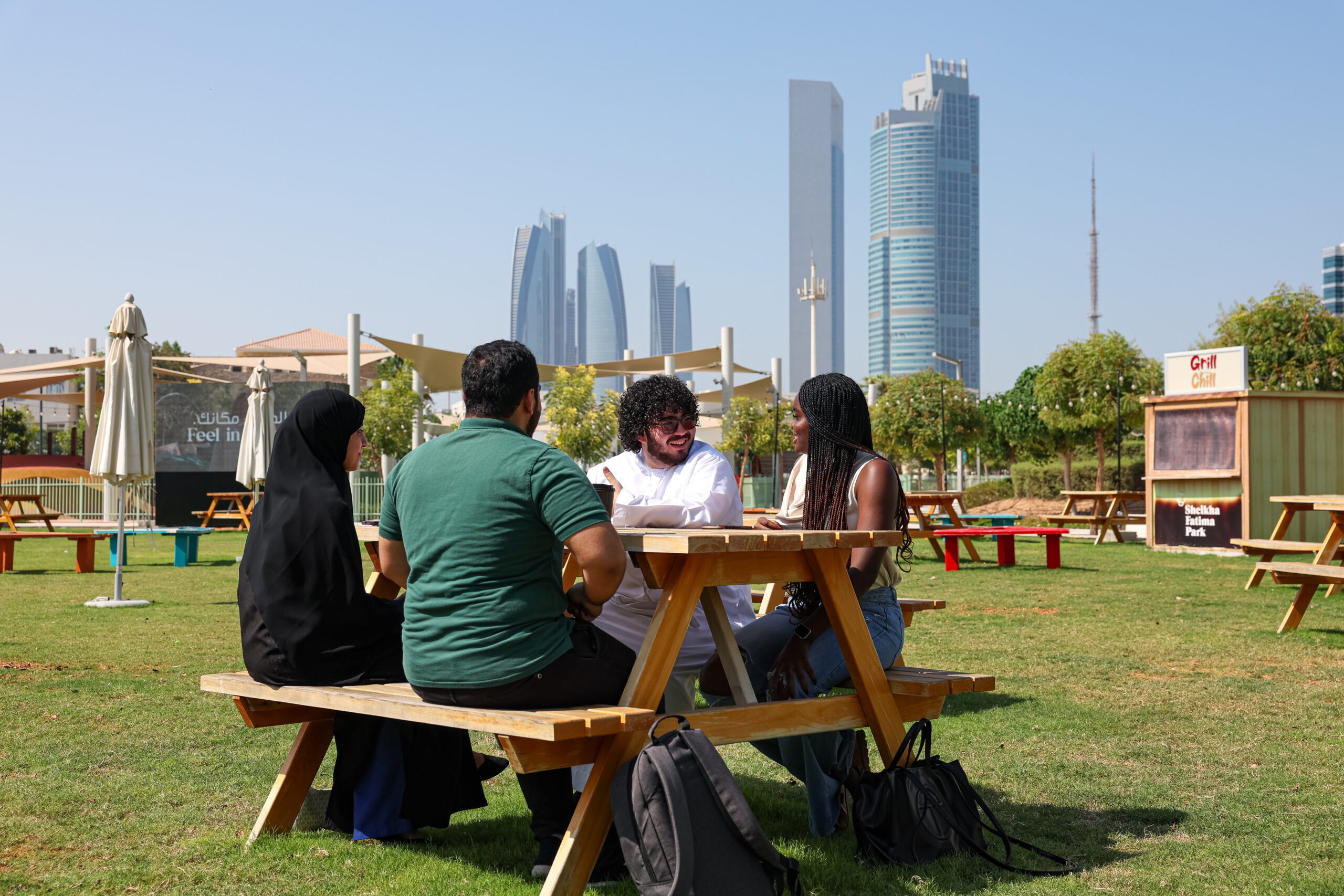 A group of students at a picnic table with the Abu Dhabi skyline in the background.