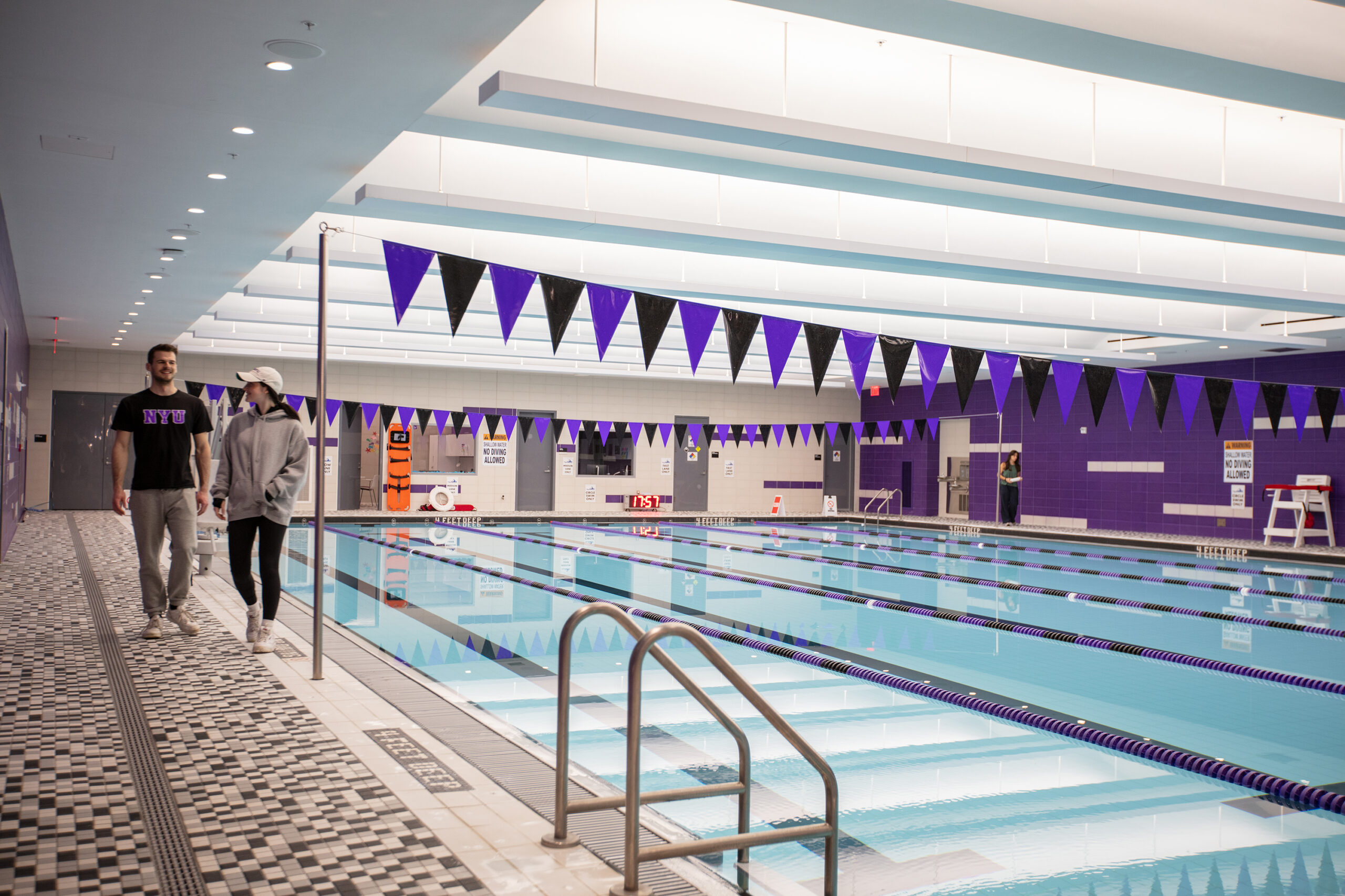 Two students walk next to a large indoor pool.