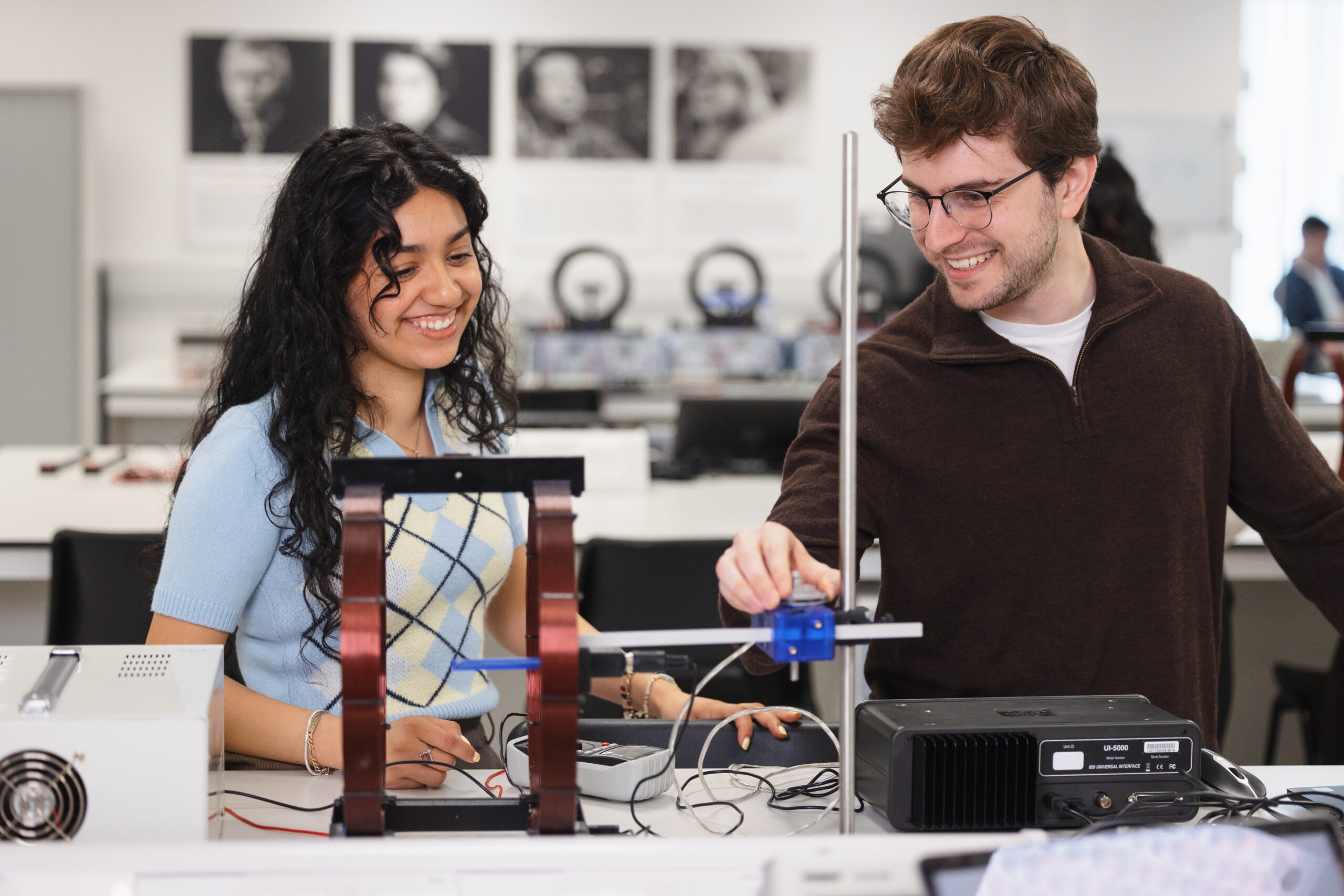 Two students work with scientific equipment at a lab table.