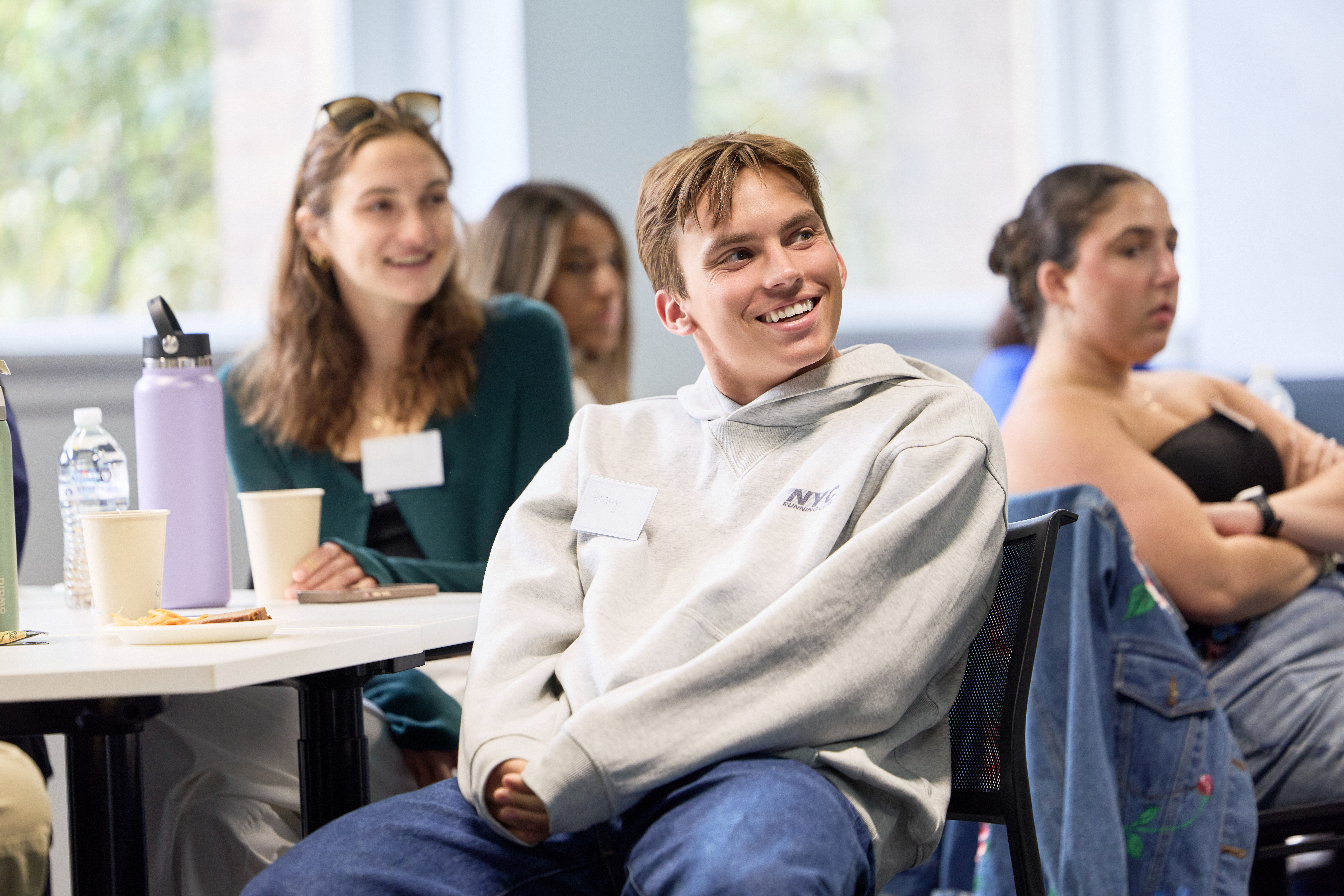 A group of students sit together smiling and listening during an orientation event.