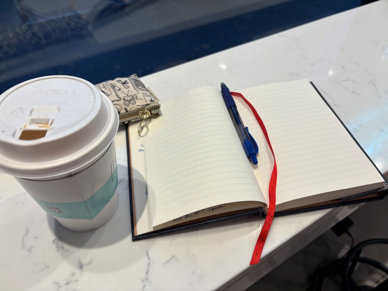 A coffee cup and open notebook on a marble countertop.