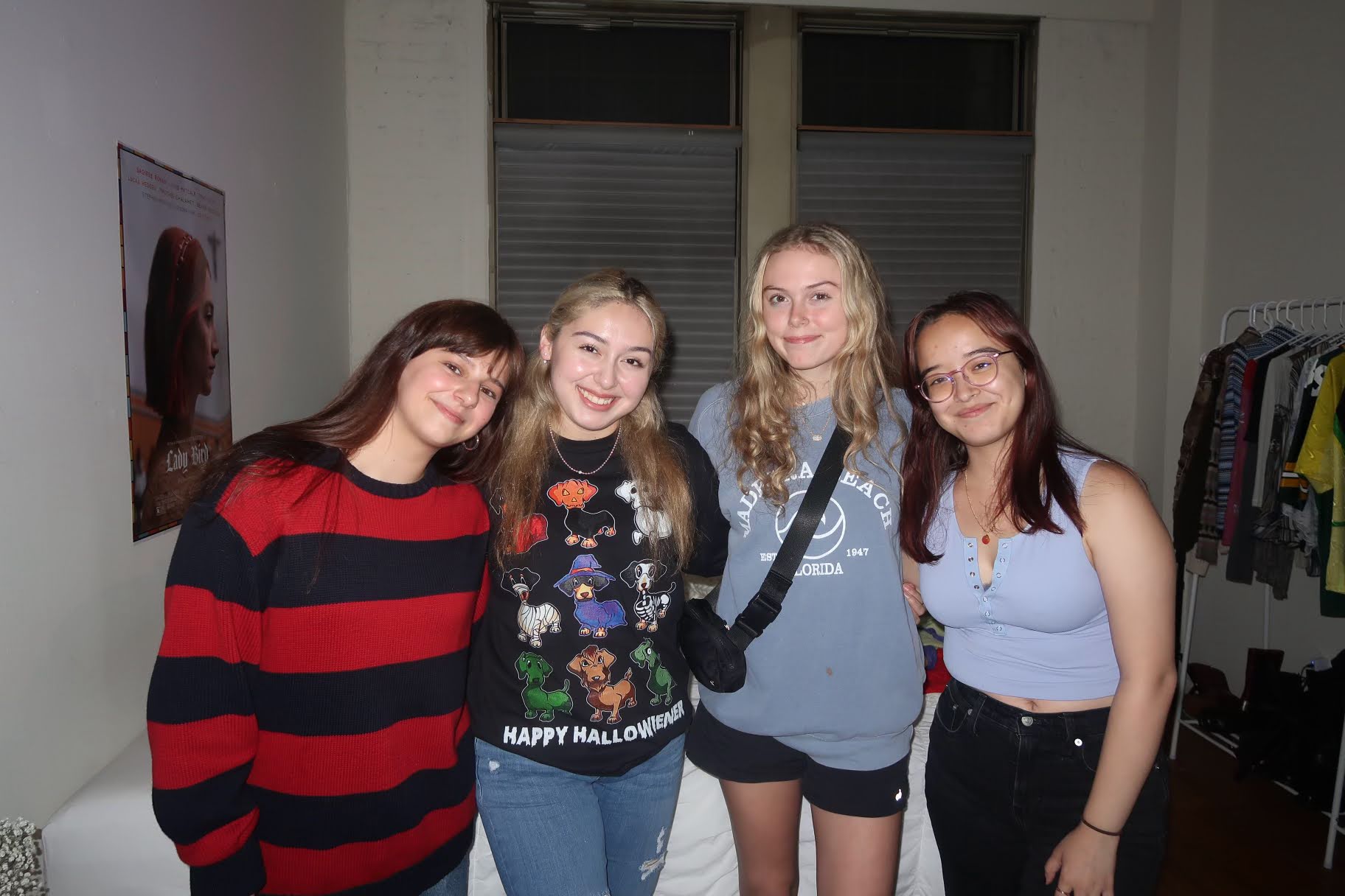 Four girls in casual clothes smiling in an apartment together.