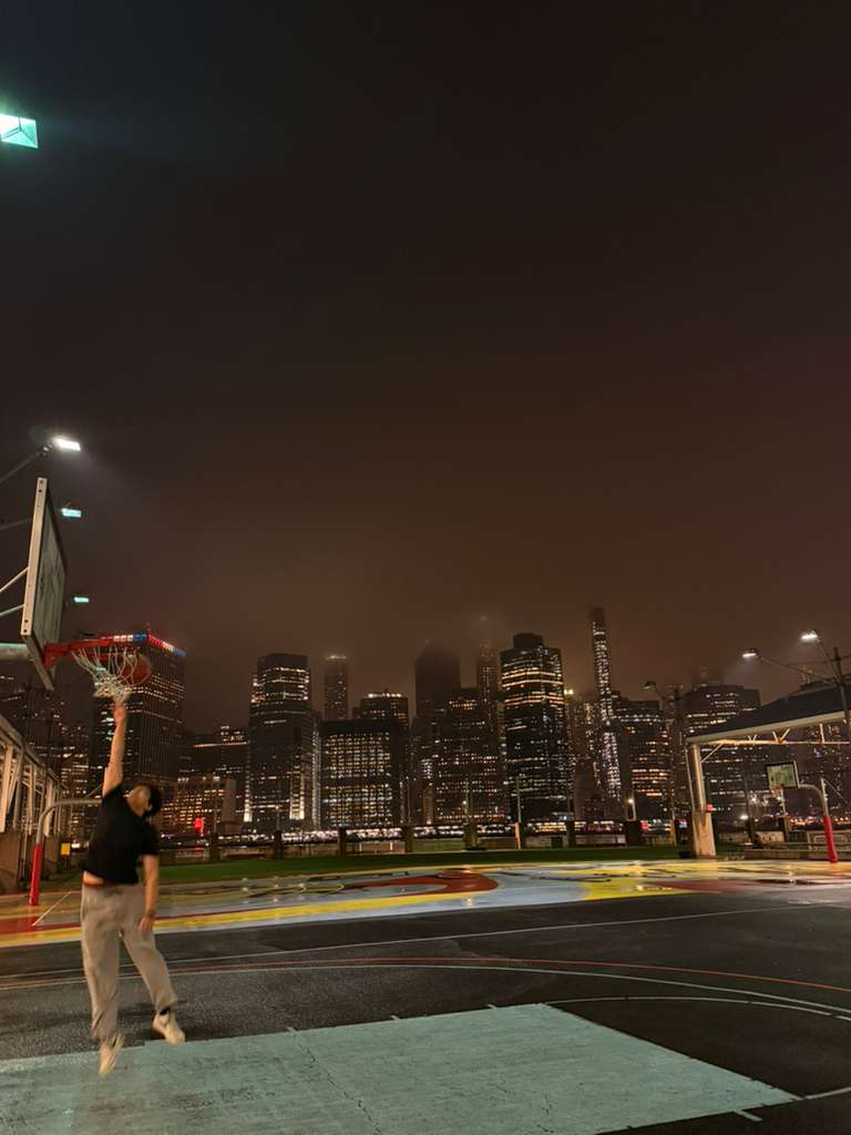 Person dunking a basketball on an outdoor court at night, with a cityscape behind them.