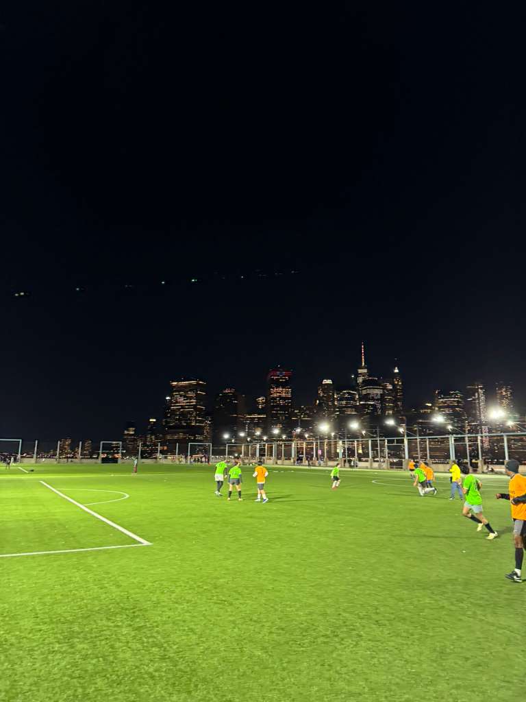 A green soccer field lit by bright stadium lights during a soccer match.