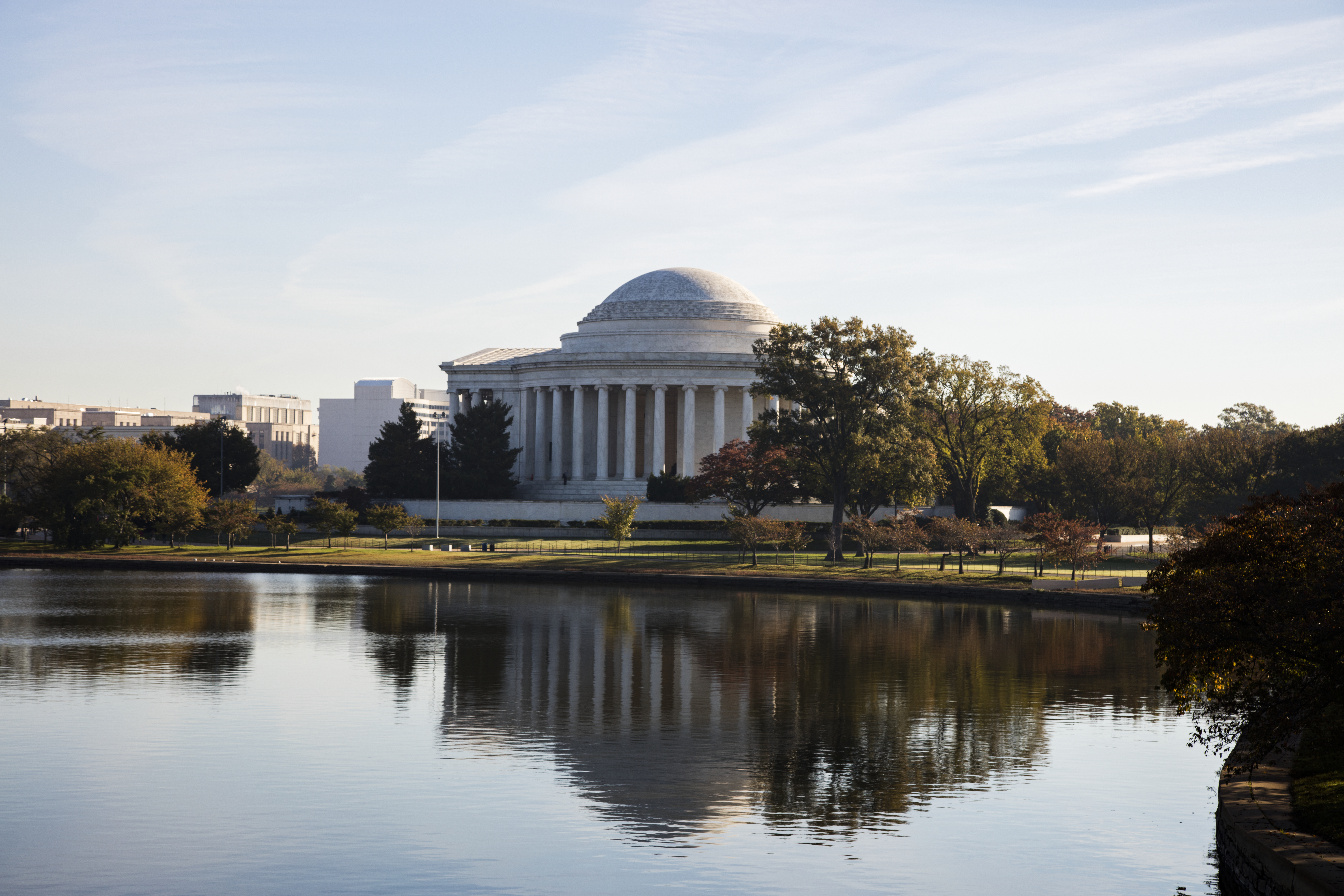The Thomas Jefferson Memorial in Washington, DC, reflected in the water of the Tidal Basin, with trees lining the shore.