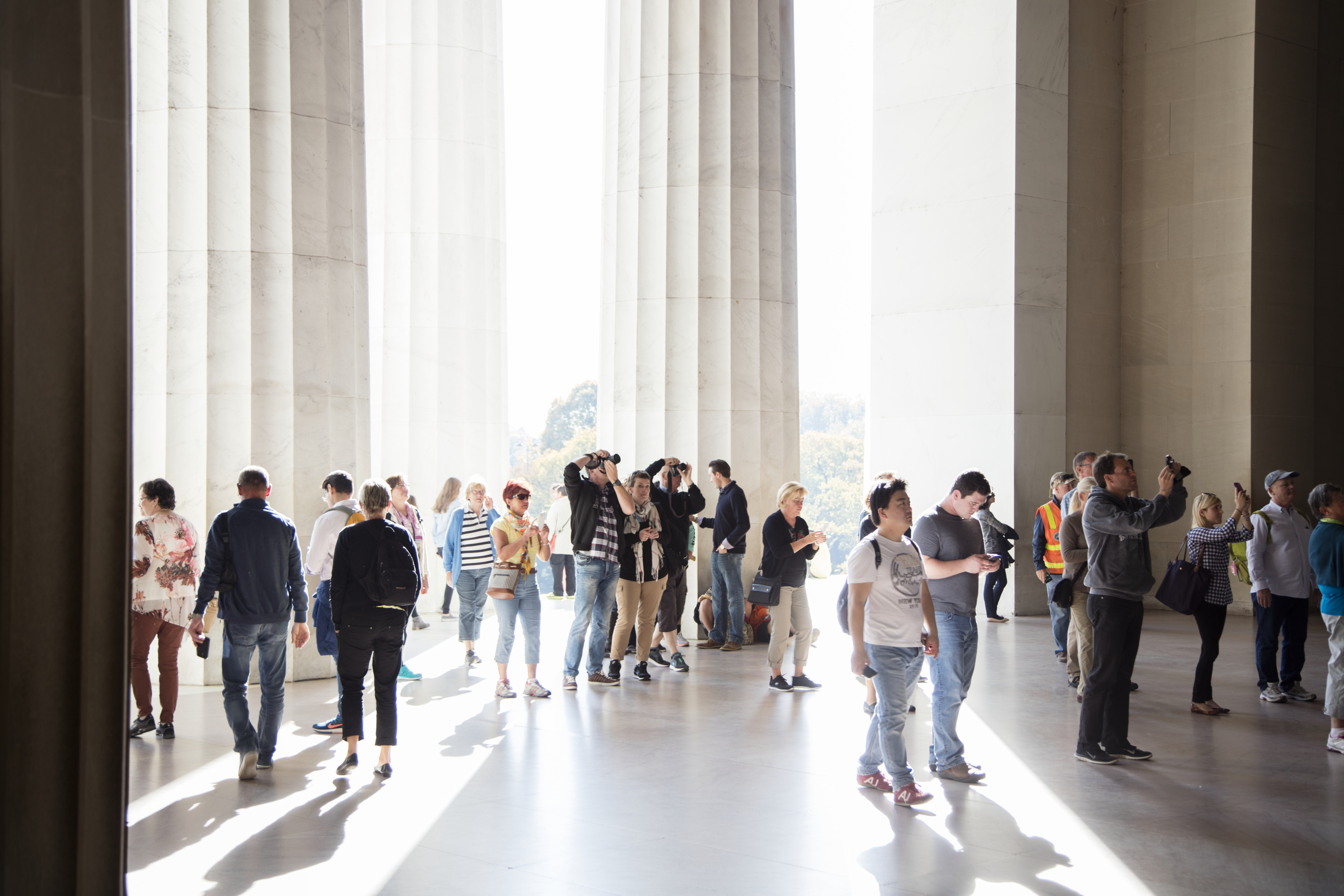 Visitors stand and walk inside the Lincoln Memorial in Washington, DC, with tall marble columns and sunlight streaming across the floor.