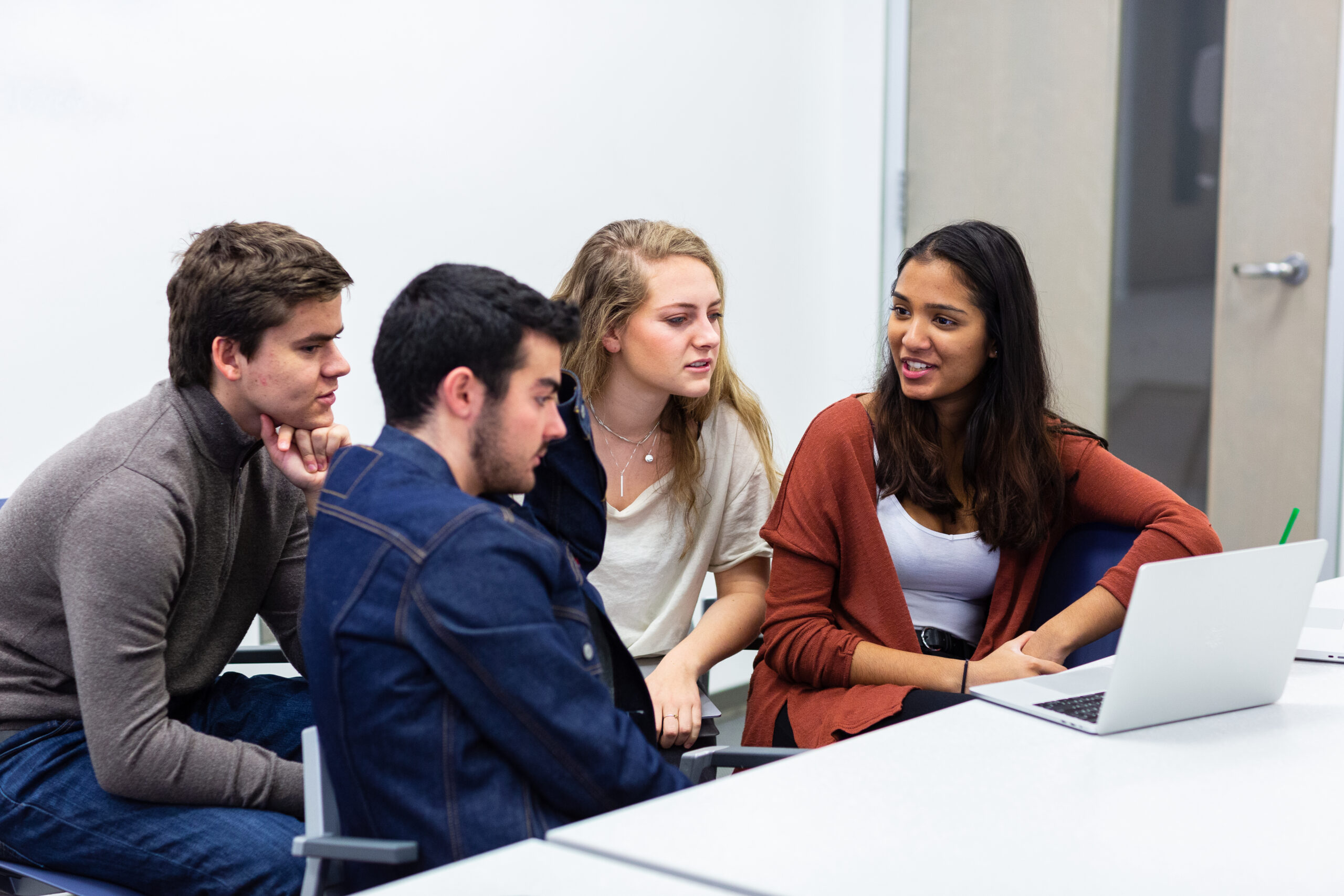 A group of students conversing around a table with a laptop on it.