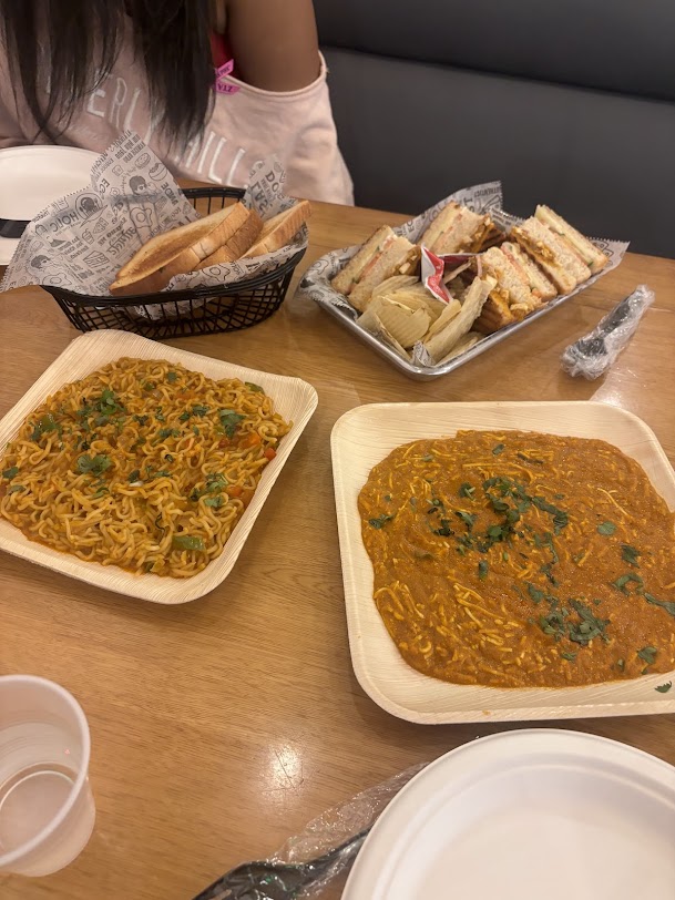 An array of 4 different Indian dishes on a table with a friend seated across in a booth.