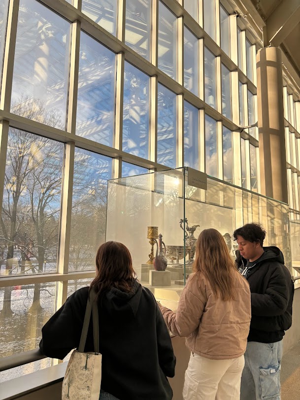 Three friends observing art at a museum with huge windows overlooking Central Park in the background.