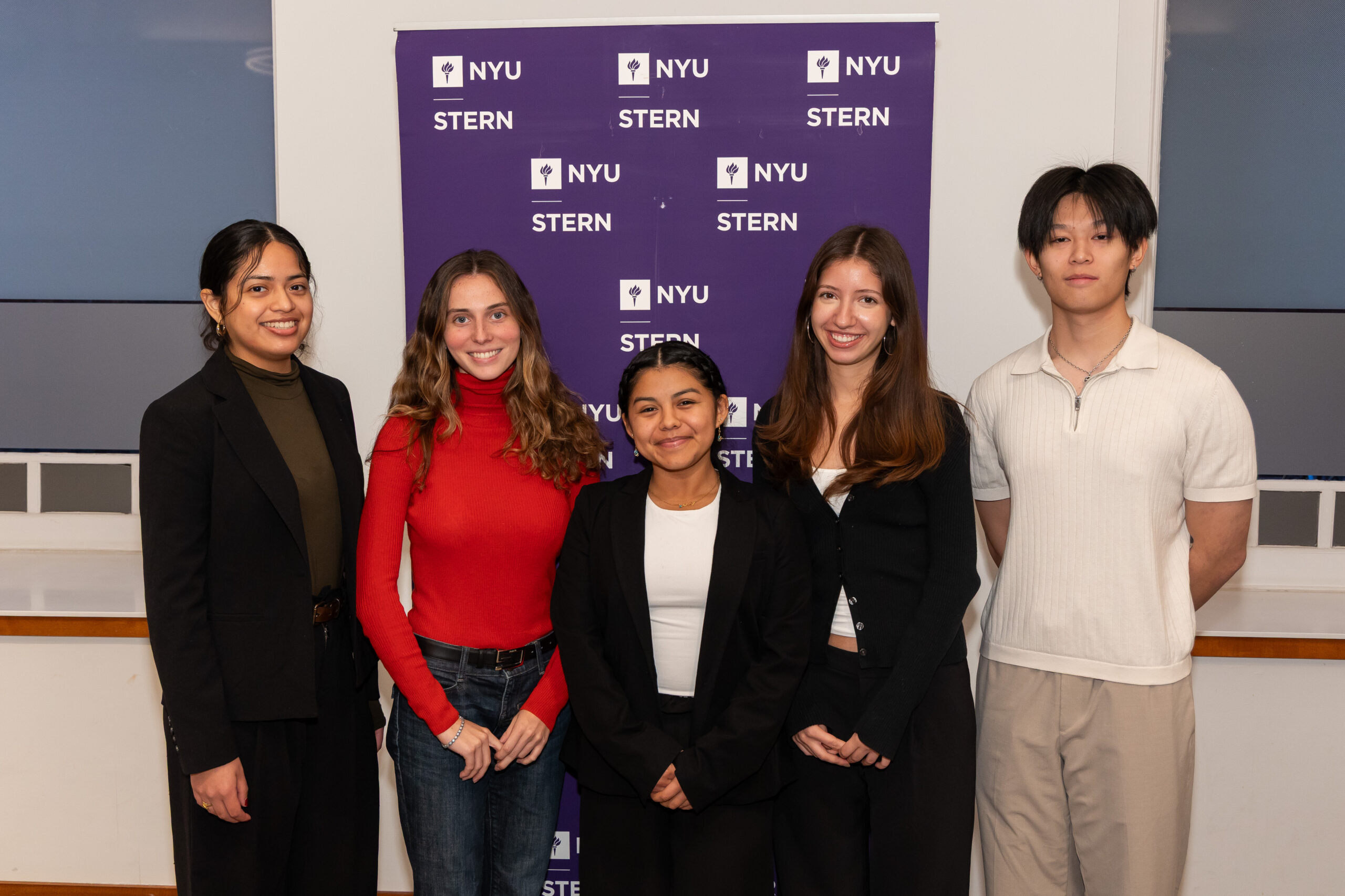 Wendy and her fellow classmates posing in front of a purple step-and-repeat that has the NYU Stern logo on it.