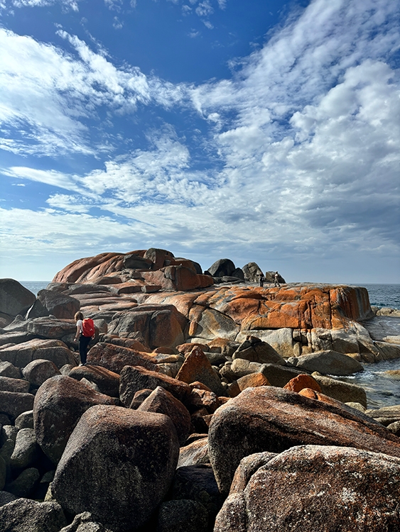 Student Angelina Gerlich walks through a large group of rocks on a shore.