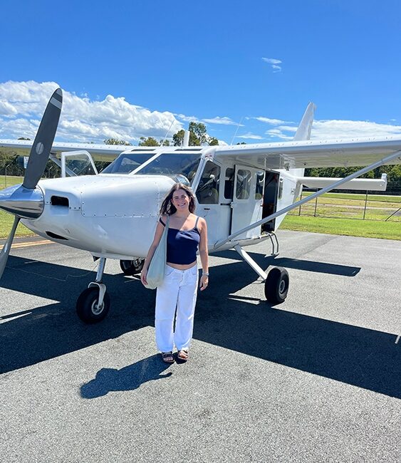 Student Isabela MacClemmy stands next to a small airplane.
