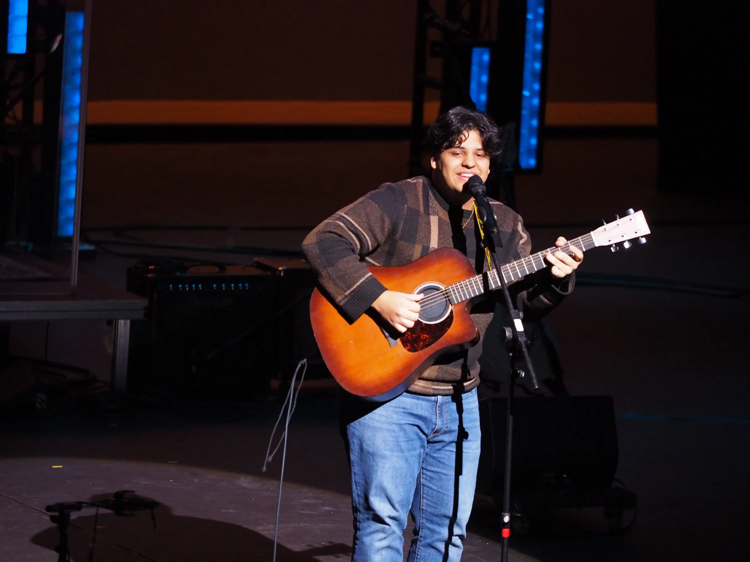 A student performing onstage with a guitar.