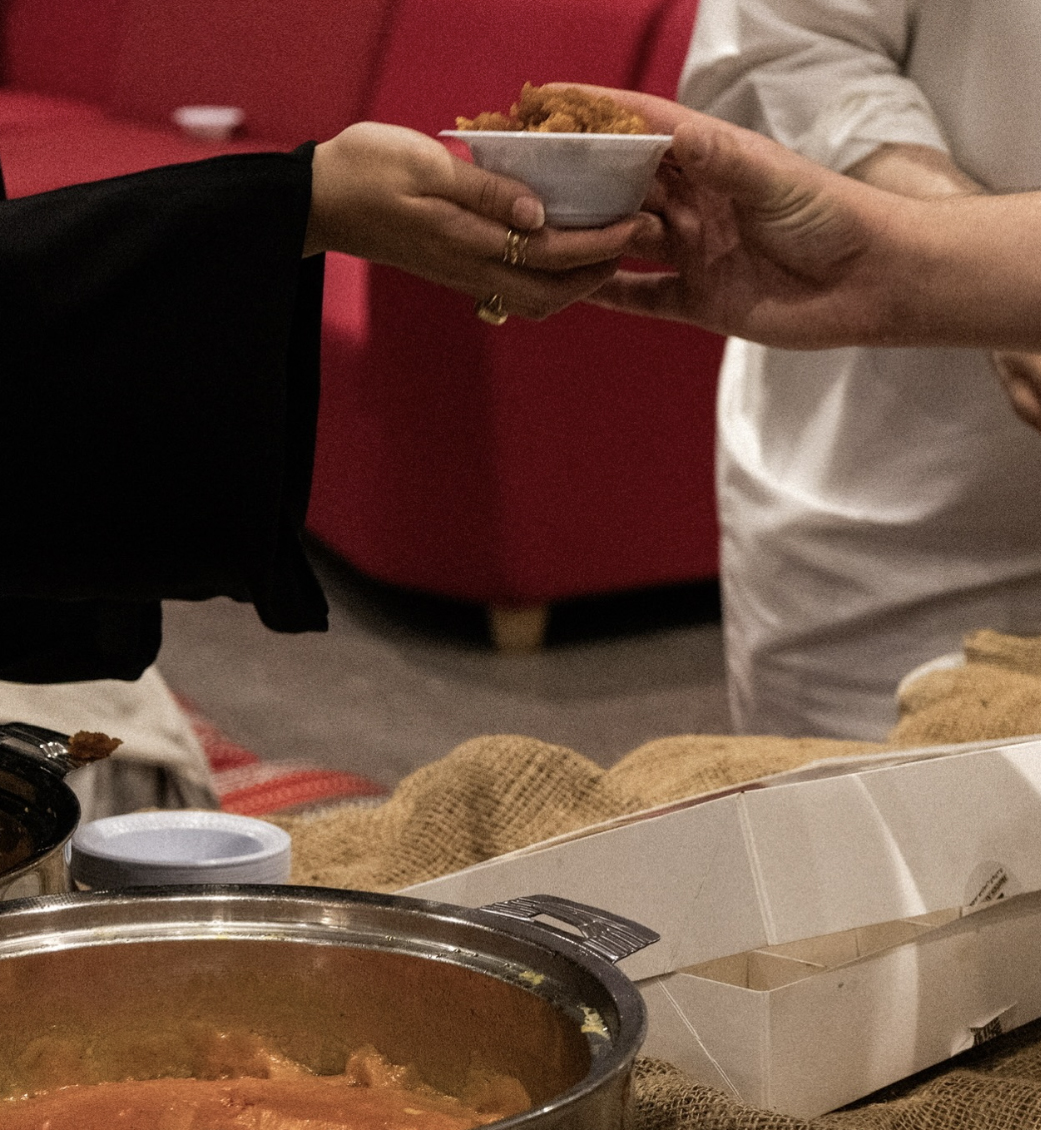 Hands pass a small bowl of food across a table set with pots and containers.