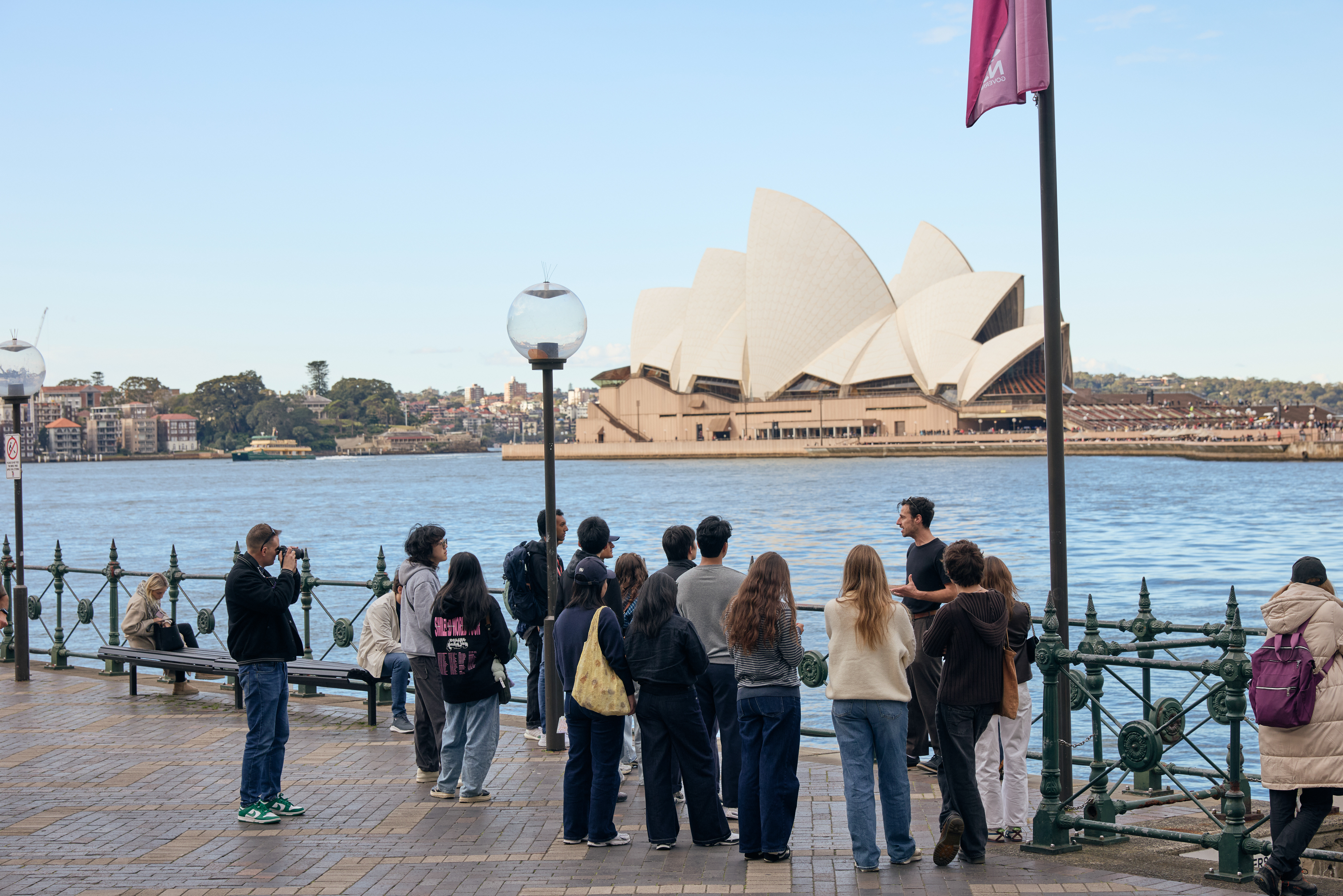 A large group of students touring Sydney, behind them sits the Sydney Harbor and the Sydney Opera House.