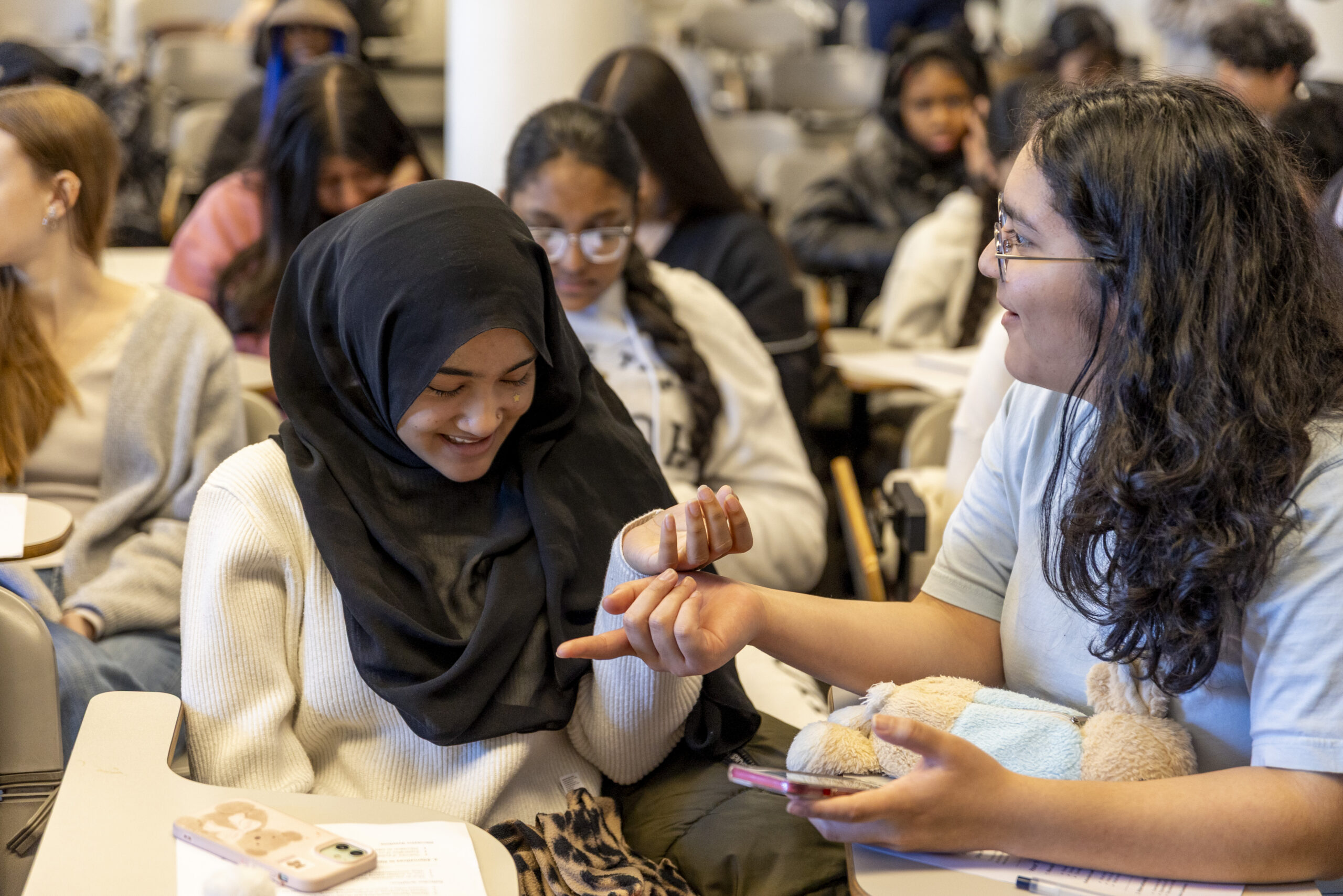Two students having a discussion in a crowded class.