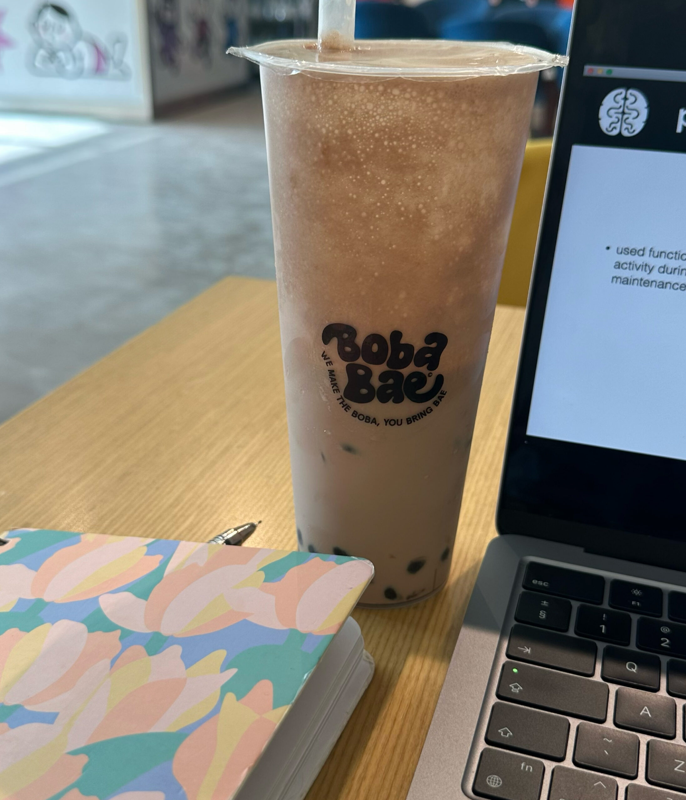 Full boba tea stands next to a laptop.