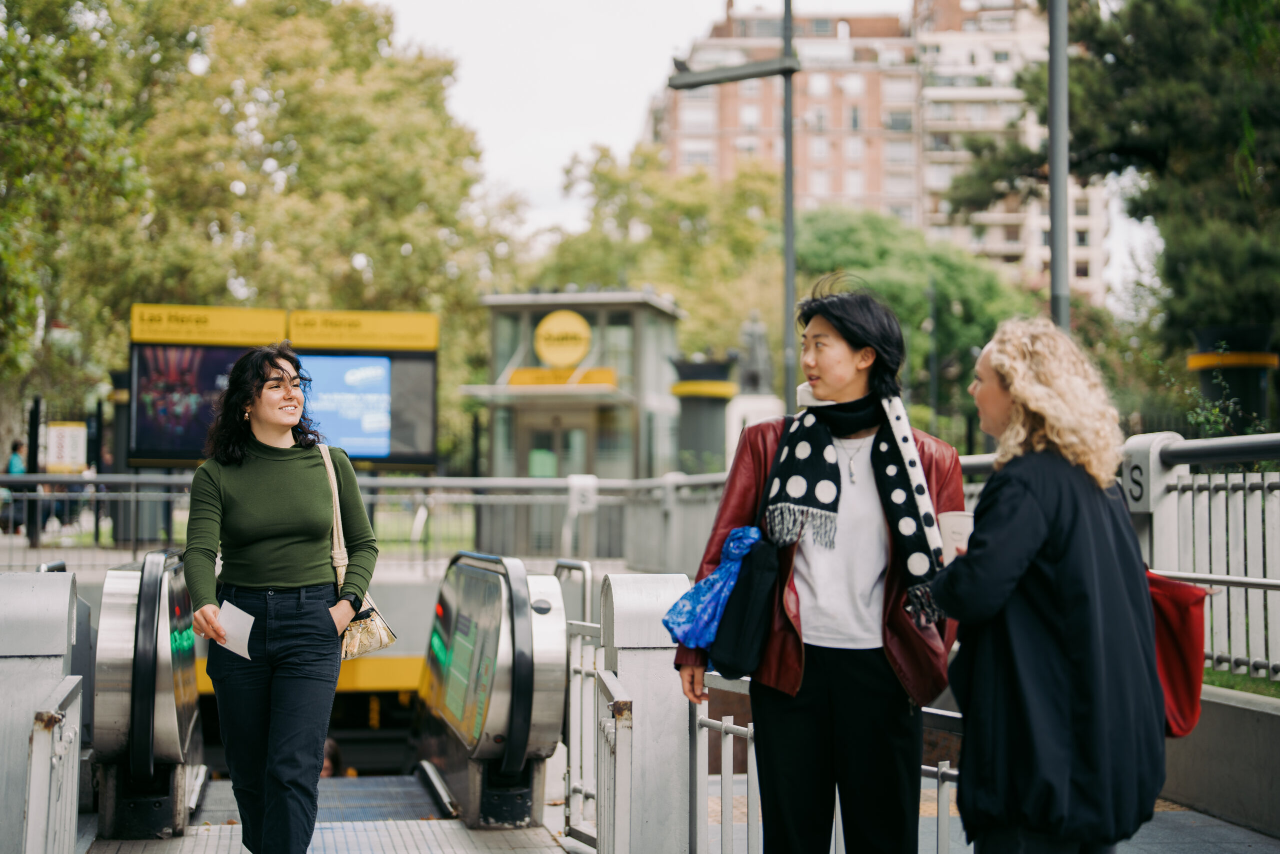 Two students turn to greet their friend exiting a subway station in Buenos Aires.