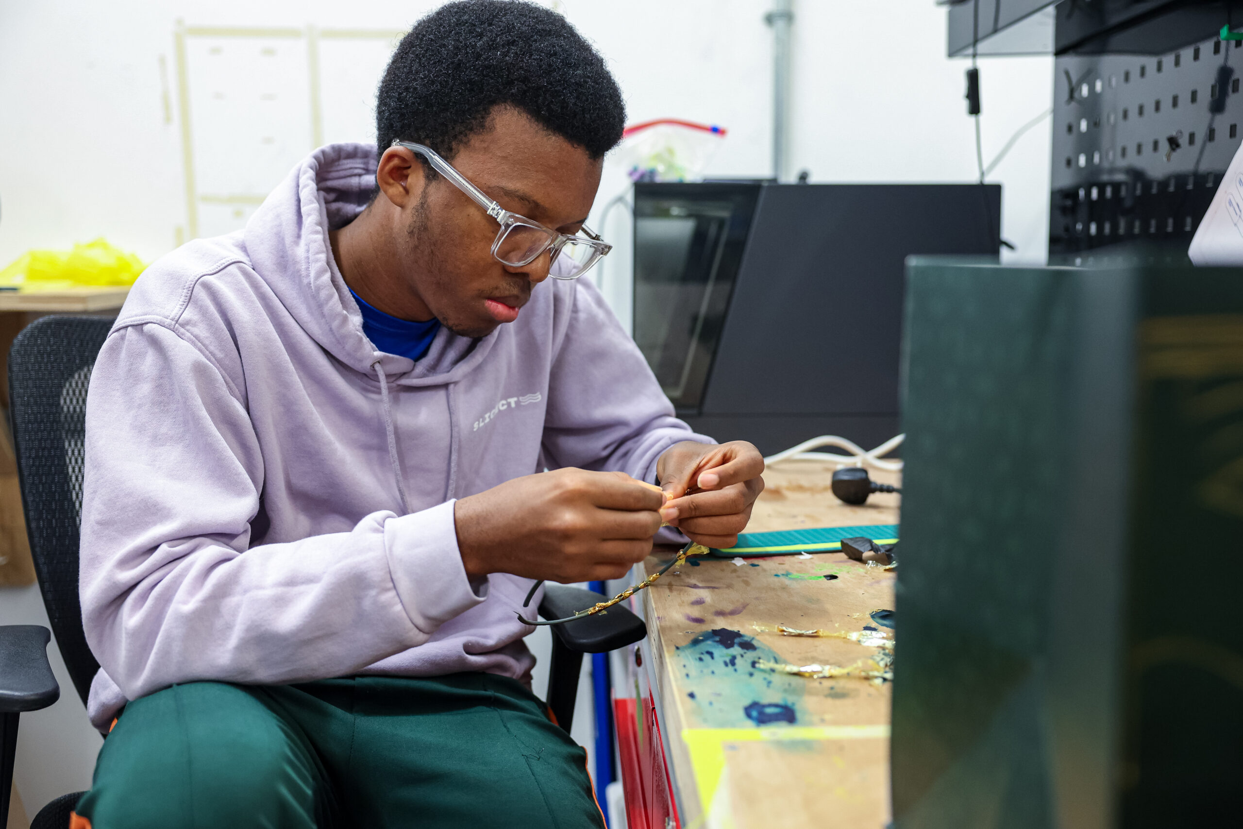 Student working carefully on a project at a workshop table, focusing on assembling small components.