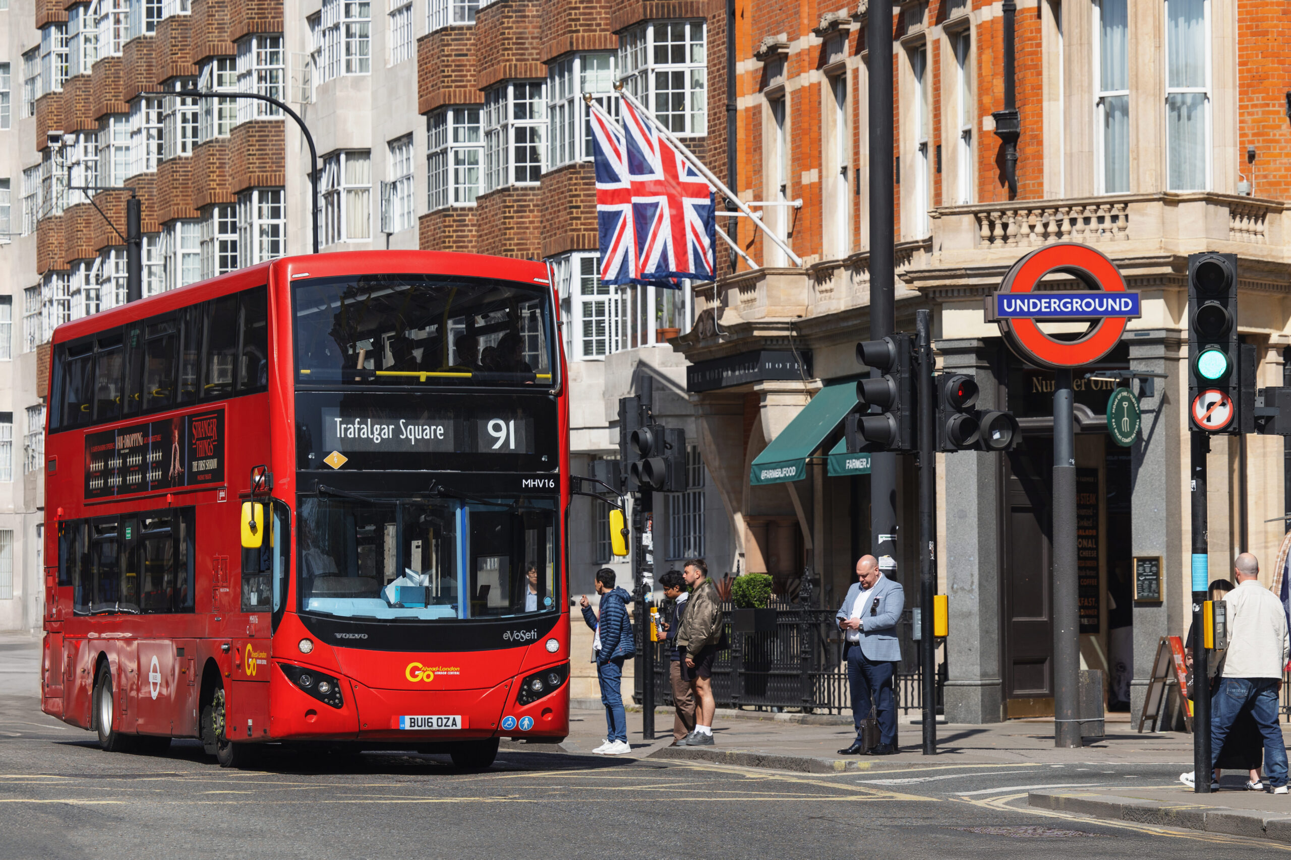 A busy street in London with people walking and an iconic red London bus passing by.