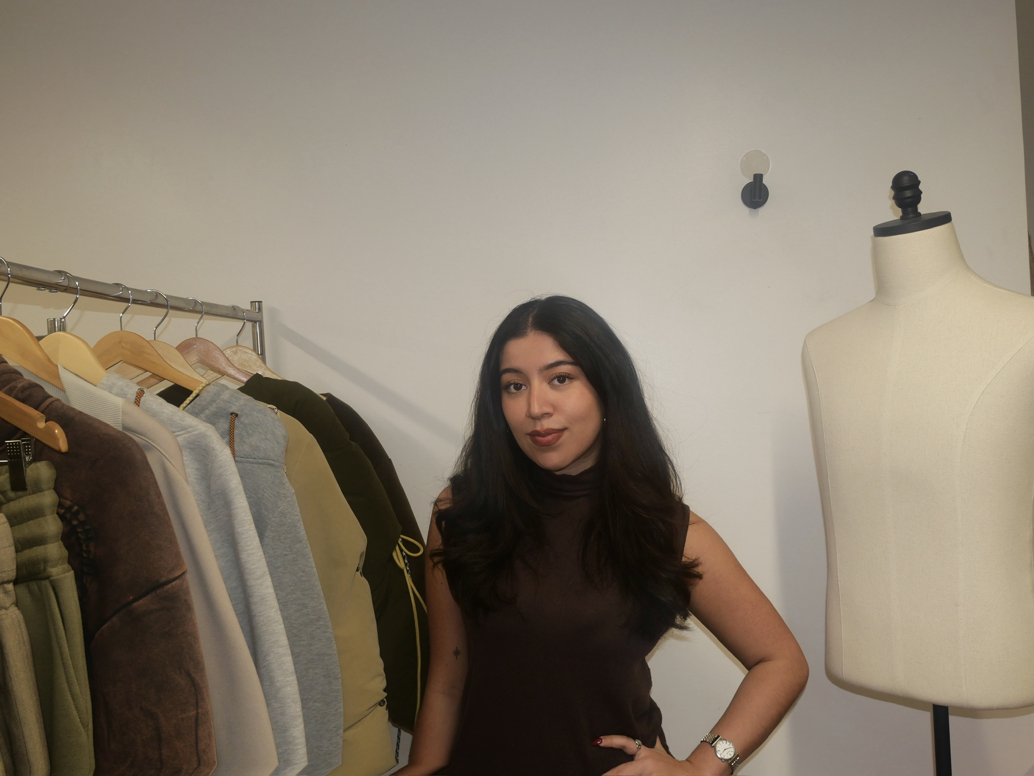 Student Daniella Leonzo posing beside a clothing rack and dress form