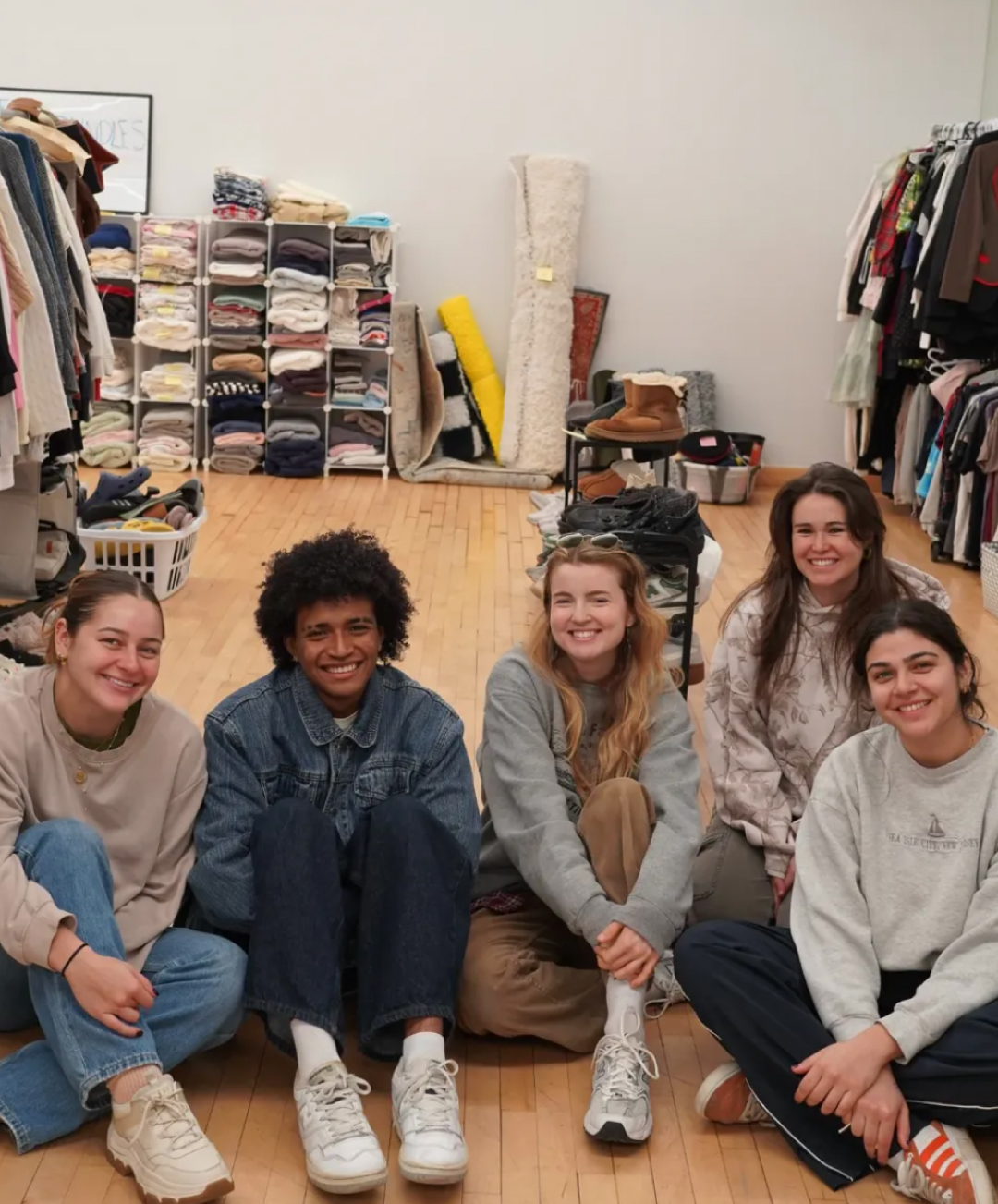 Students seated and surrounded by available clothing and goods at the NYU Swap Shop.