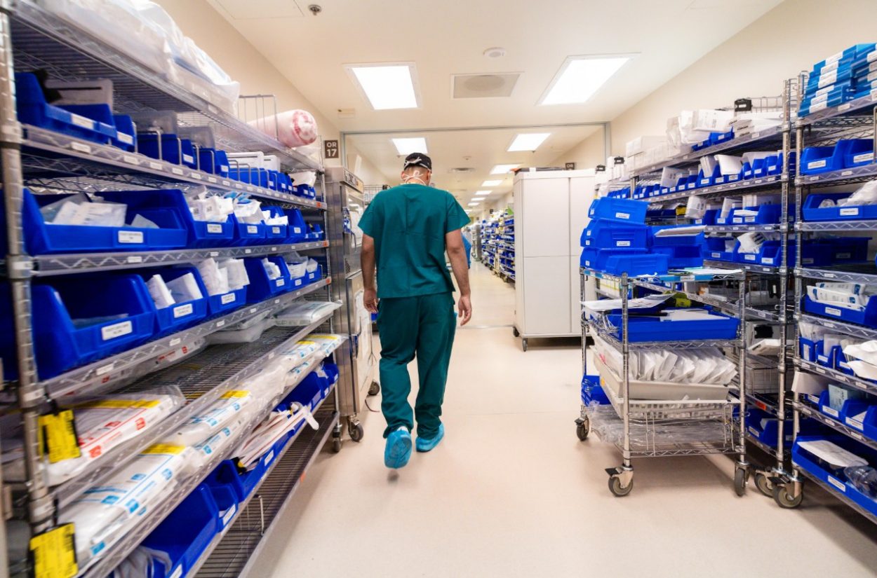 Massimo walks between racks of medical supplies.