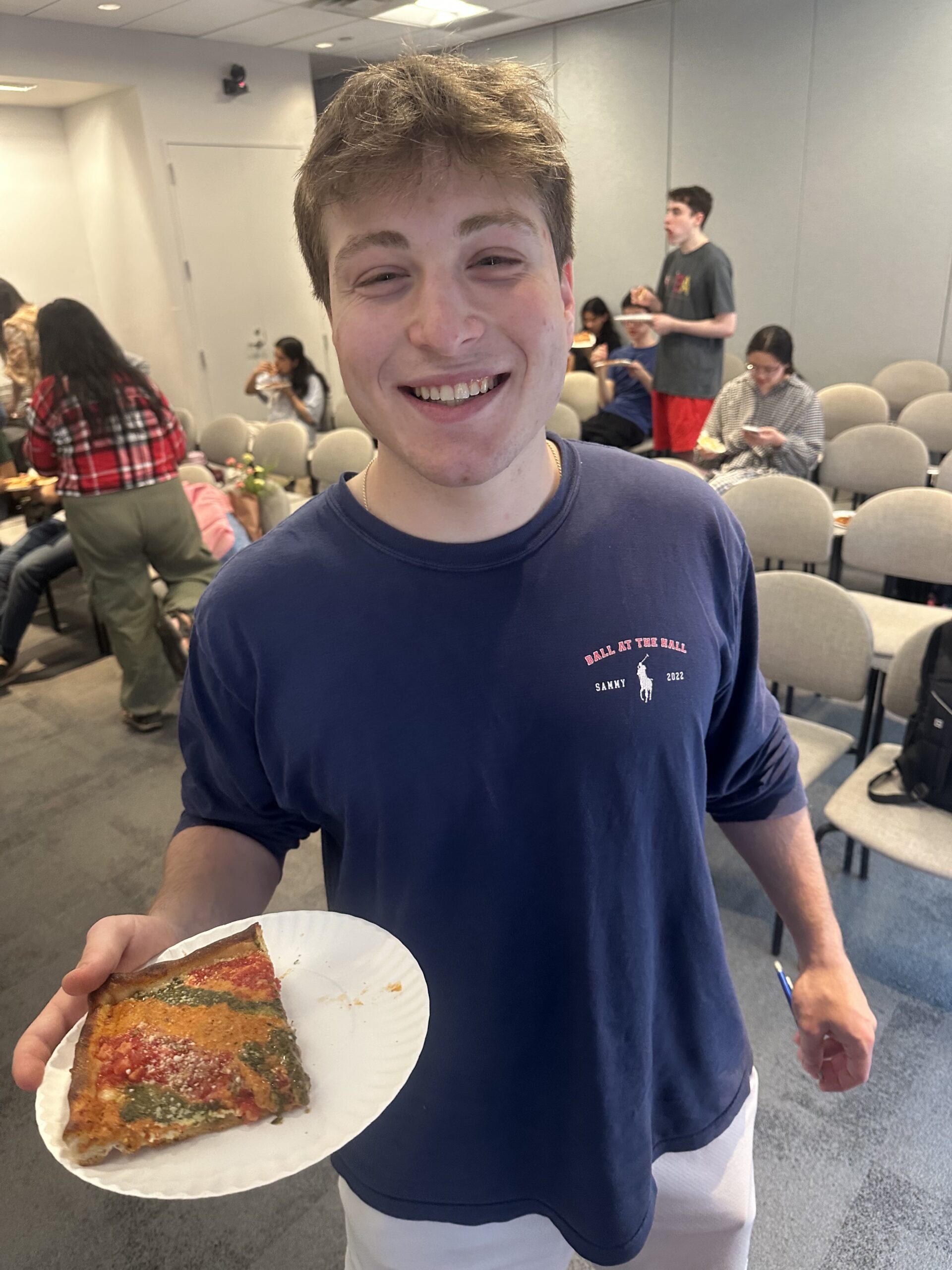 A student holding a slice of pizza during an NYU Pizza Club meeting.