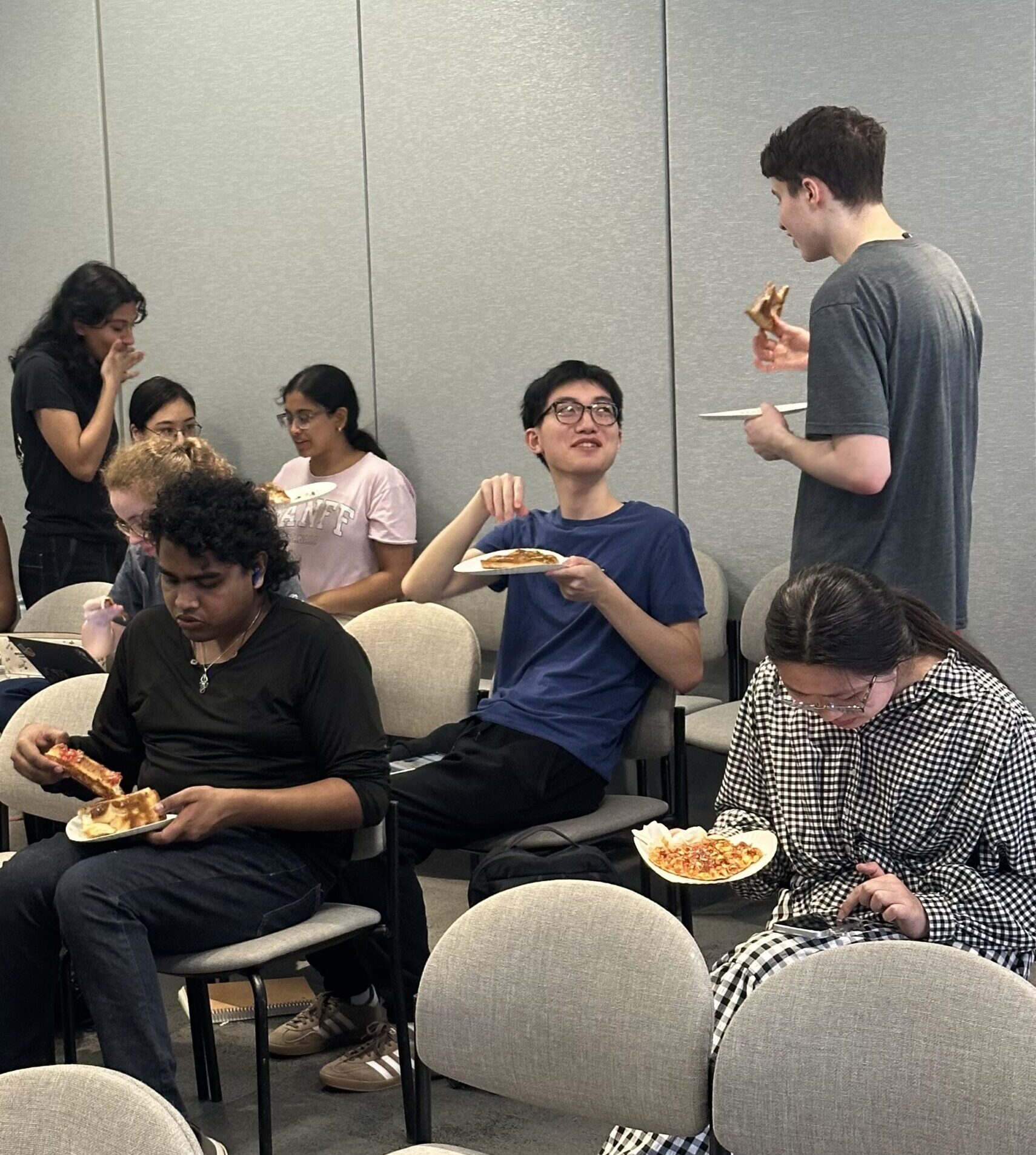 Students eating pizza and talking during an NYU Pizza Club meeting.