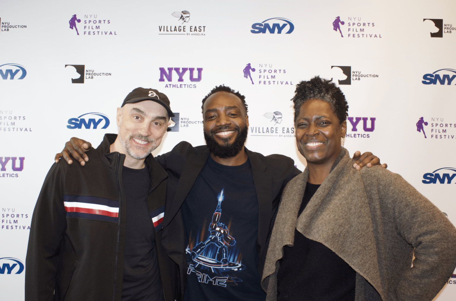 Three attendees smiling and posing together in front of an NYU Sports Film Festival step-and-repeat backdrop.
