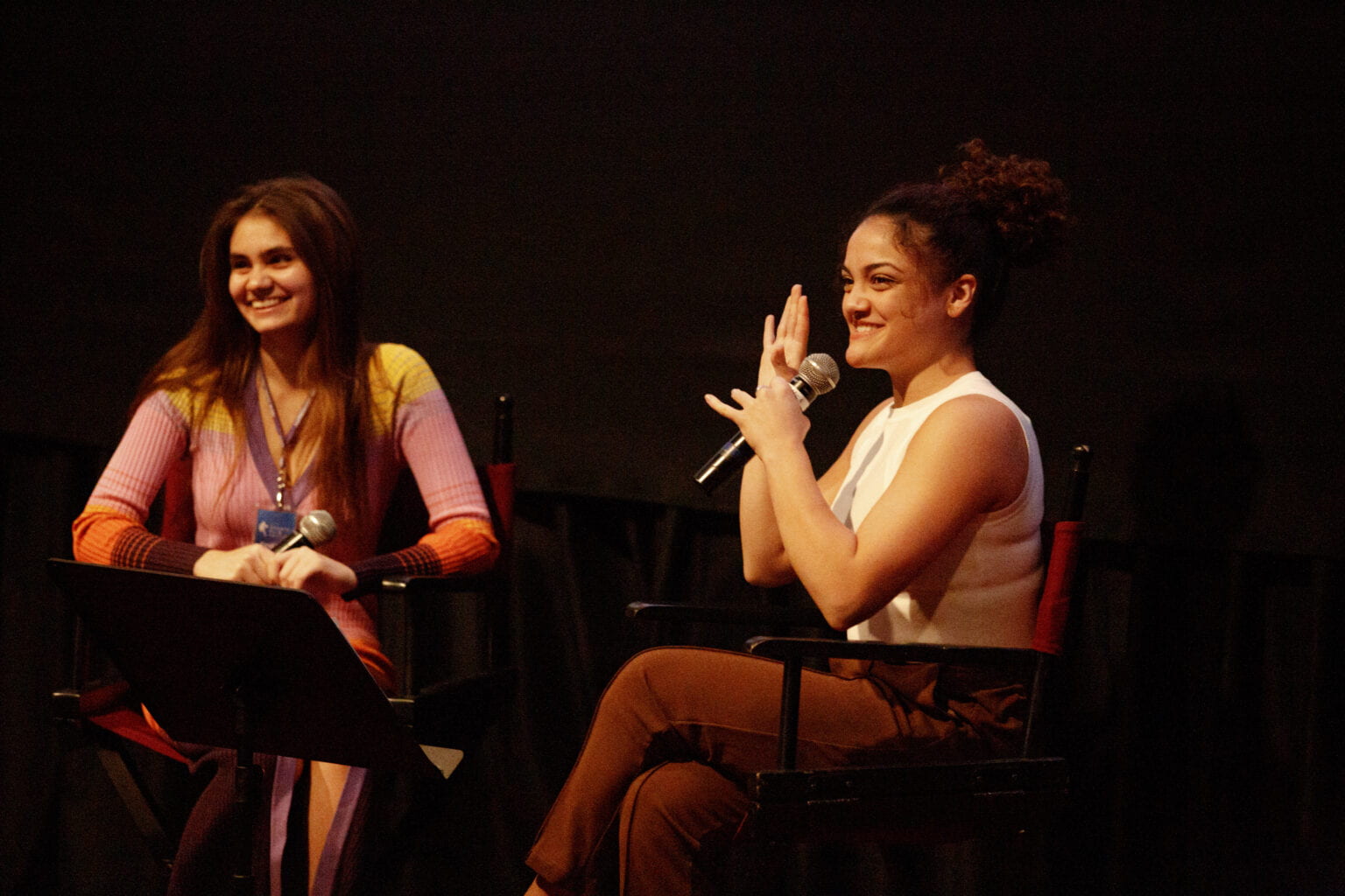 Two speakers seated on stage at the NYU Sports Film Festival, smiling and holding microphones during a discussion.