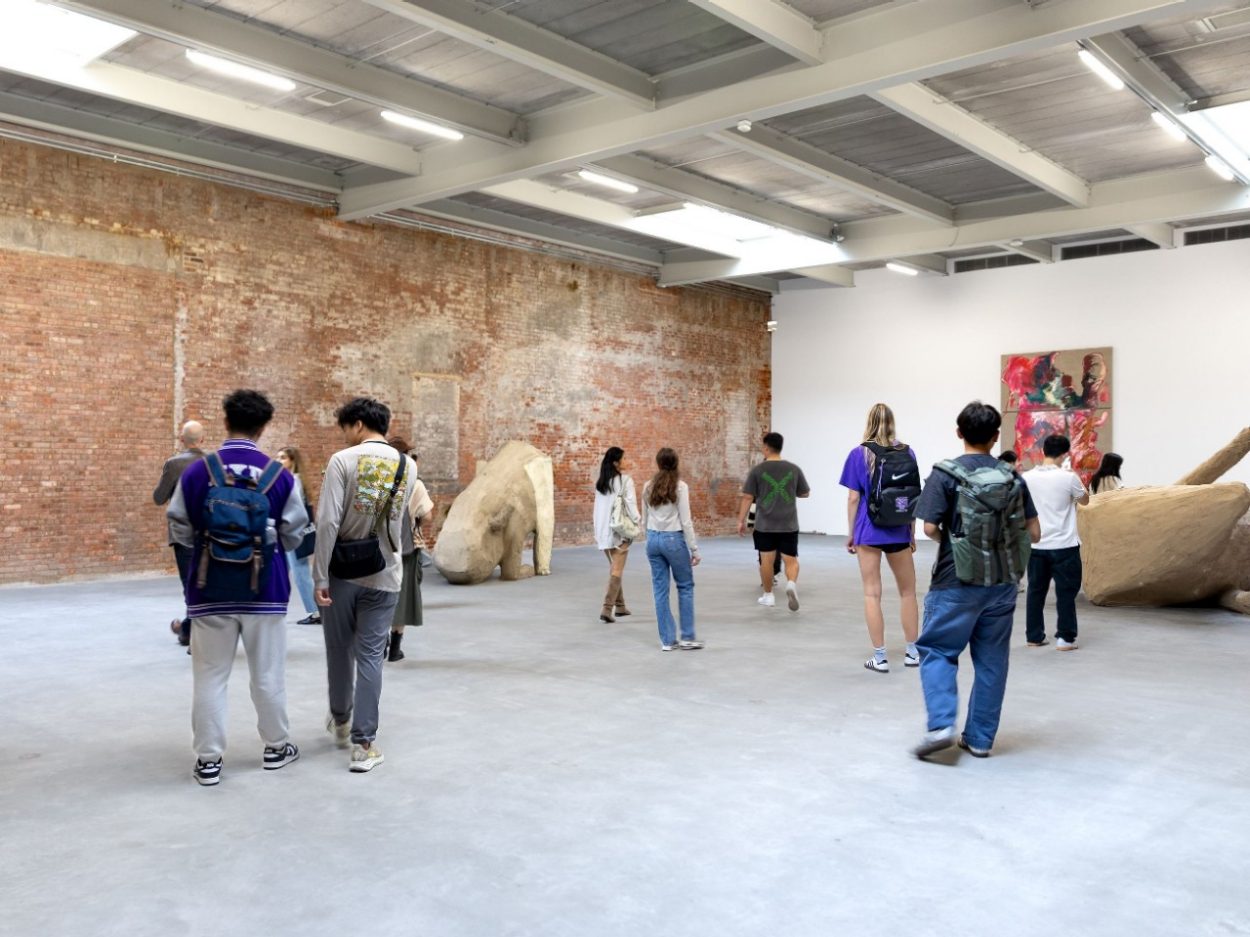 People standing at various points in a gallery room, with objects of art interspersed throughout.