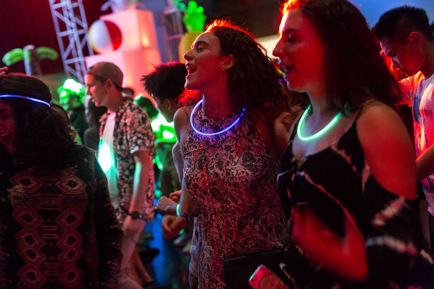 Students dance and enjoy a campus social event under neon lights.