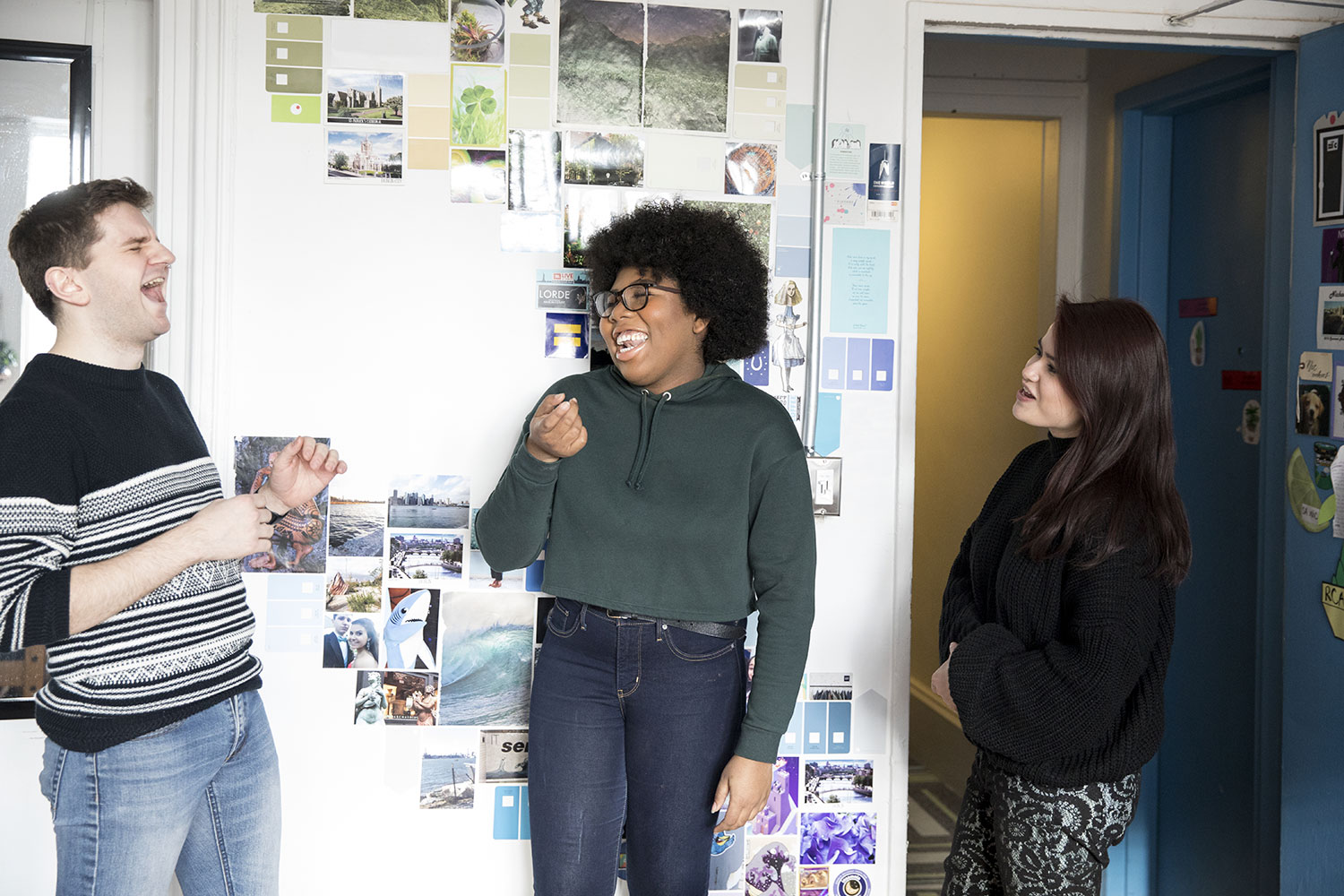 Three students laugh together inside a decorated dorm room.