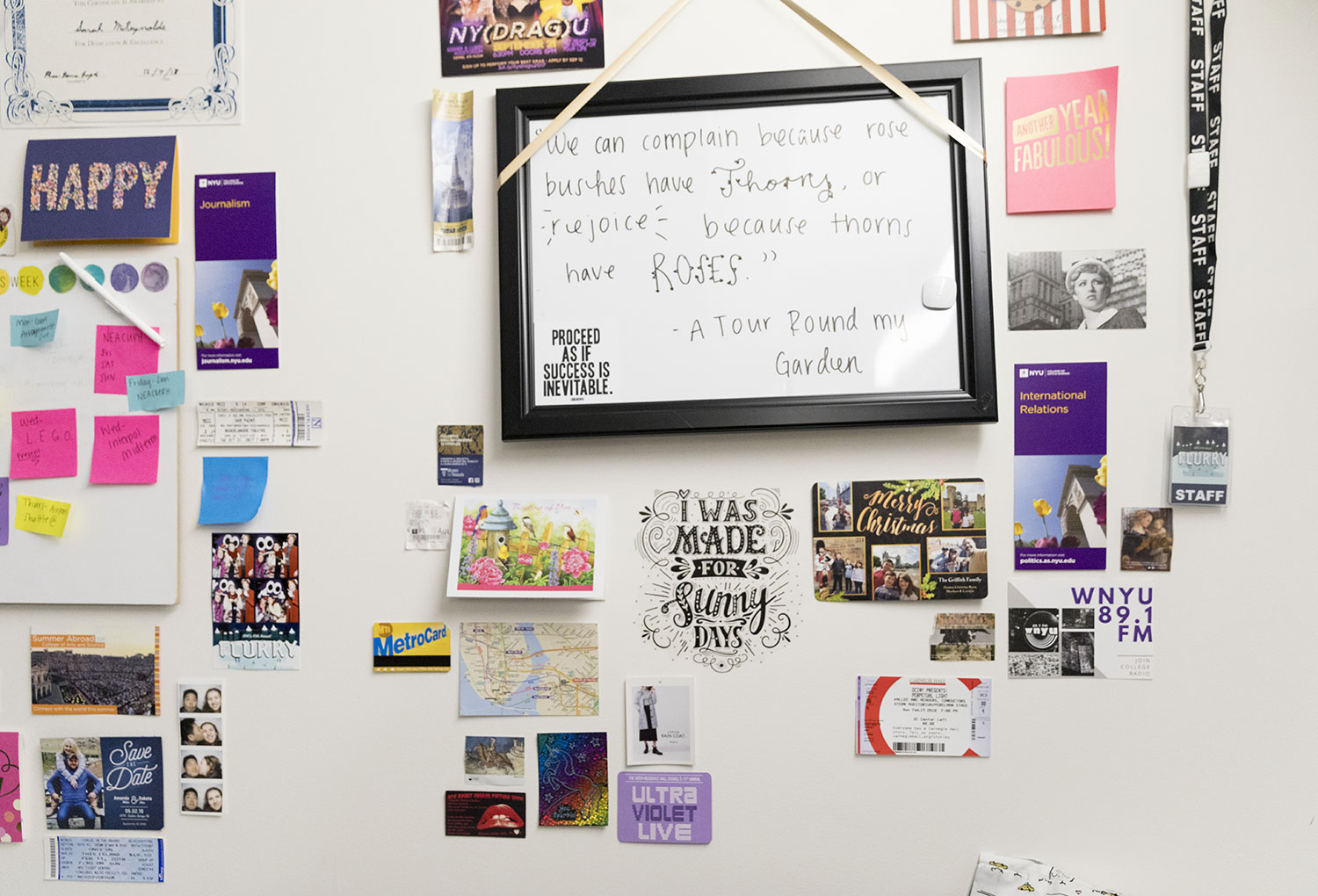 A residence hall wall decorated with personal photos, postcards, event tickets, and campus memorabilia surrounds a framed whiteboard.