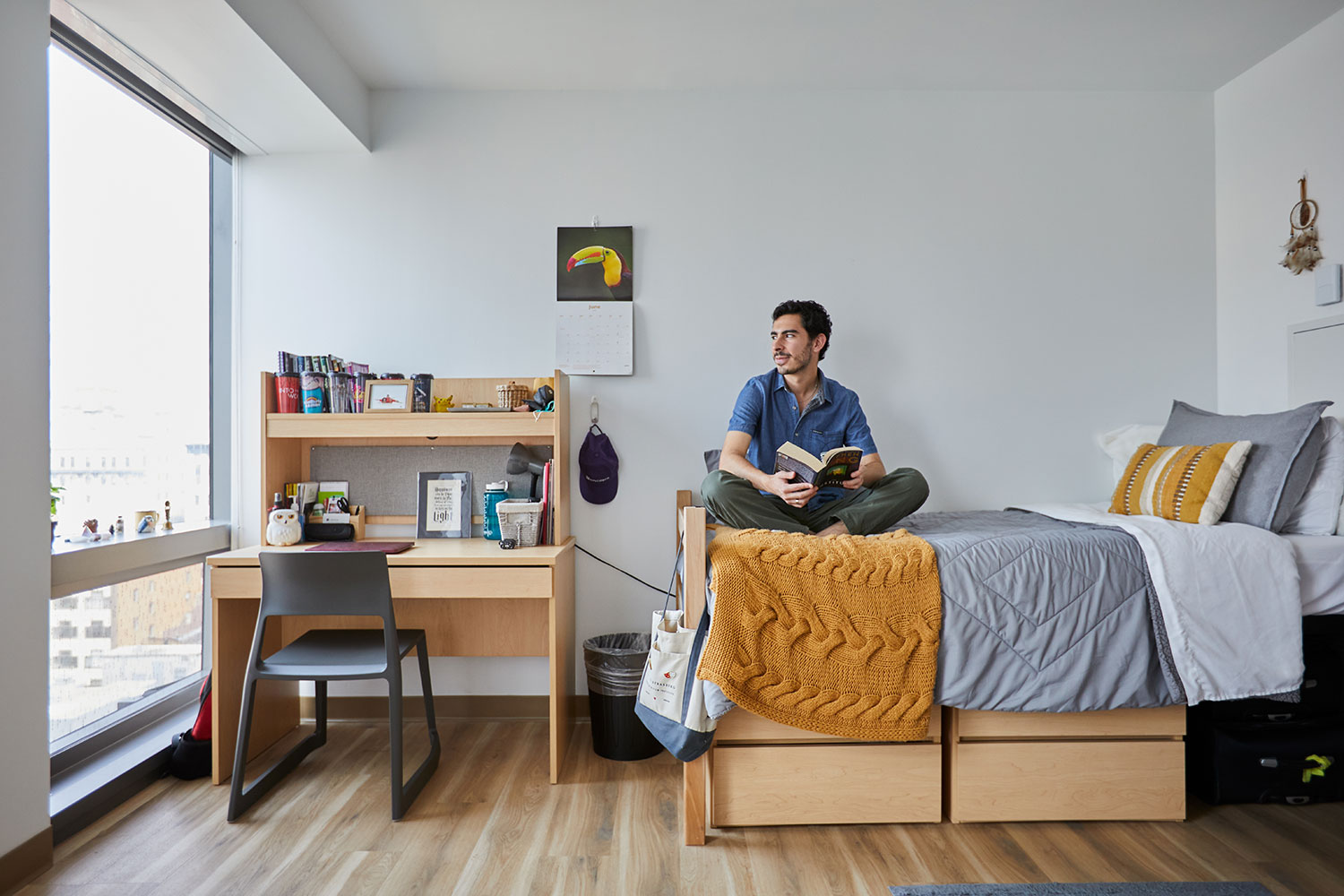 A student reads on the bed in a bright residence hall room.
