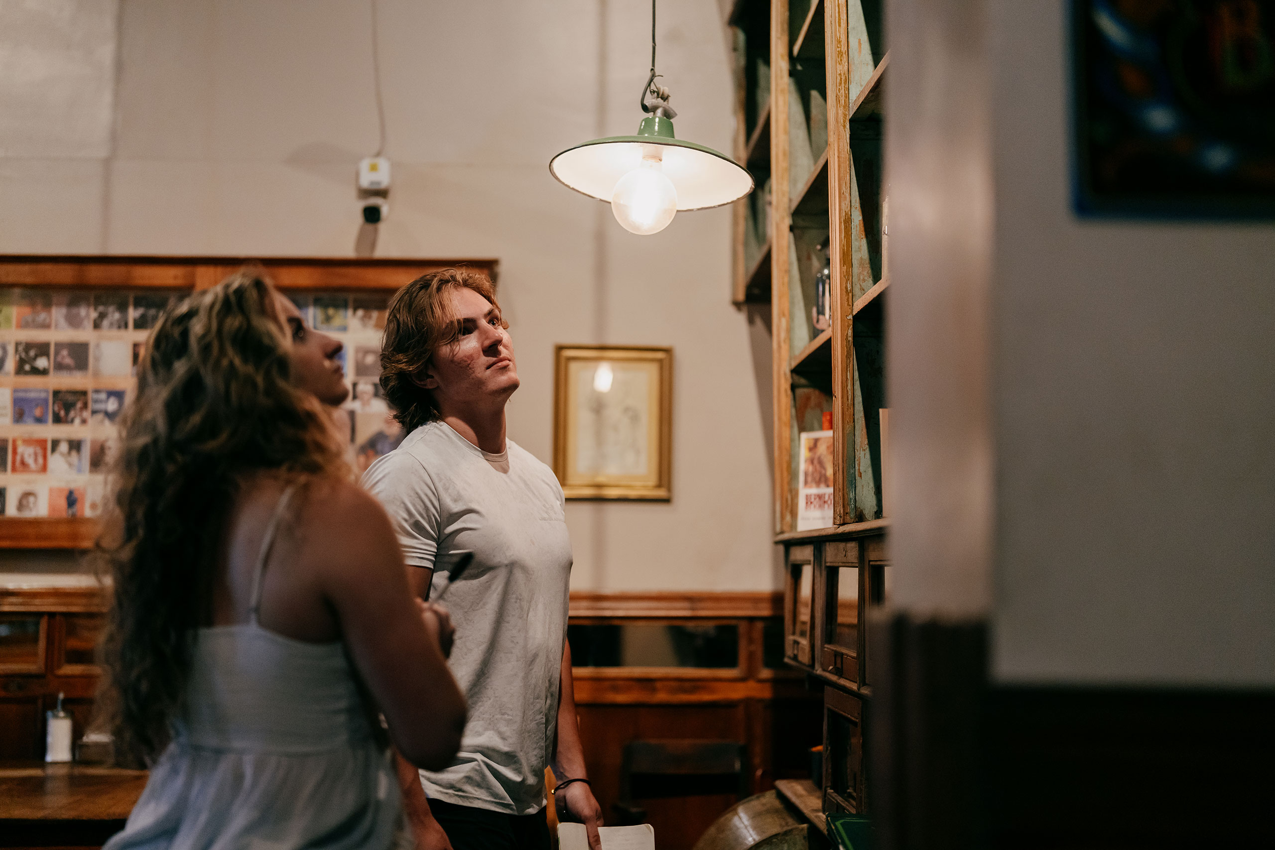 Two students standing inside a cafe in Buenos Aires, looking up at a tall display shelf filled with books and knick-knacks.