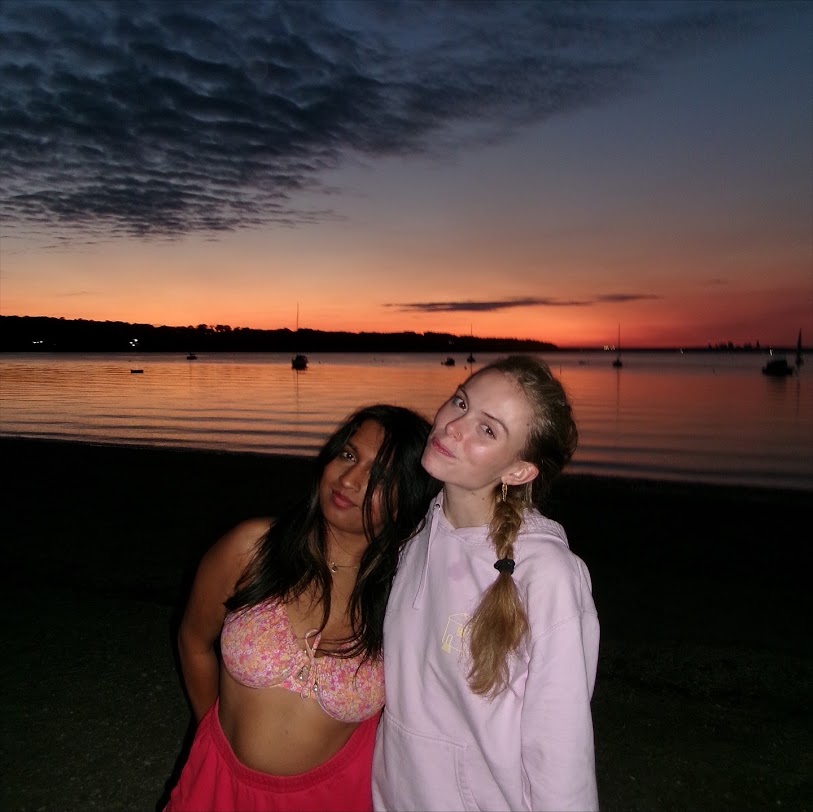 Two girls smiling and posing together on a calm beach at sunset.
