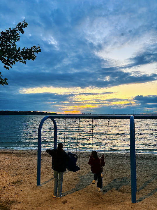 Two friends on a beach at sunset, one is swinging on a swing set.