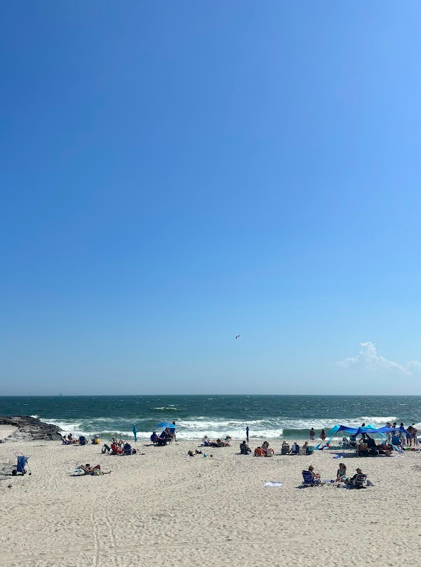 A sunny beach with people sitting on towels & umbrellas.
