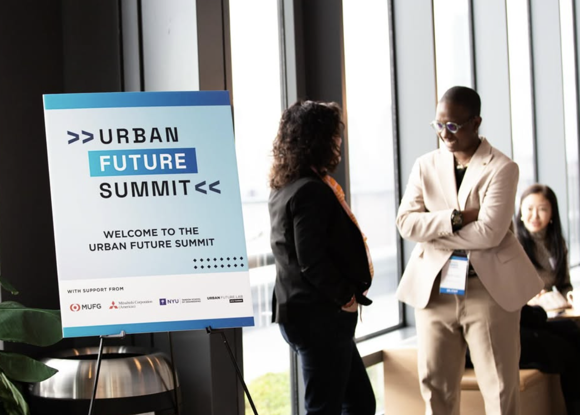 Two attendees converse beside a sign welcoming guests to the Urban Future Summit.