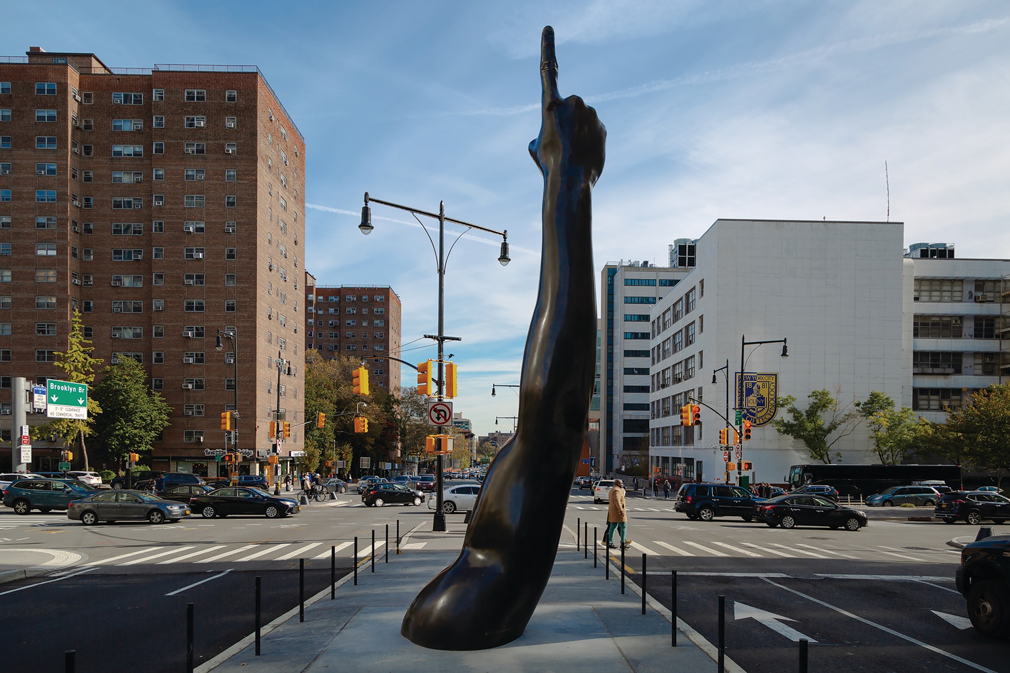 Unity by artist Hank Willis Thomas, a large sculpture of an outstretched arm with its index finger pointing upward, stands in the center of a busy New York City intersection.