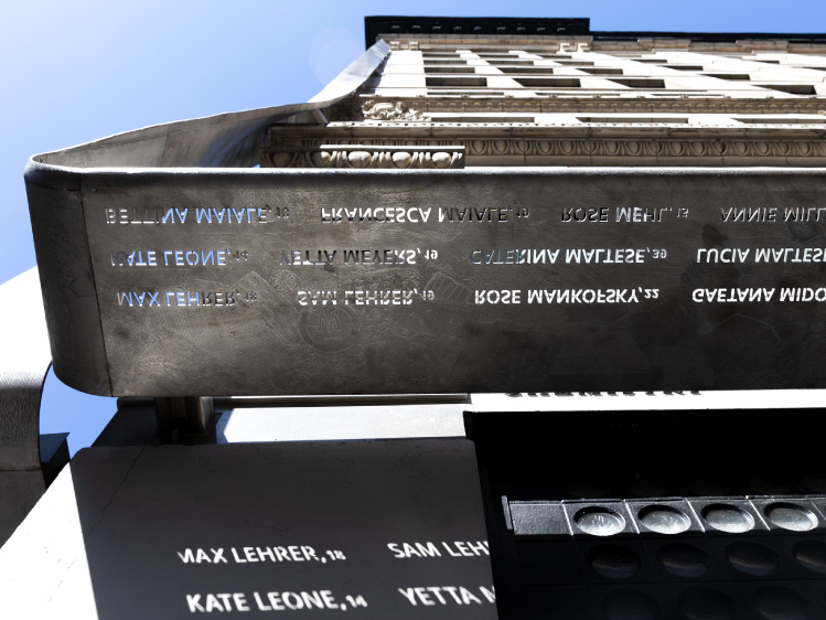 The Triangle Shirtwaist Factory Memorial features the names of the victims etched into a long steel beam mounted along the building's exterior, commemorating those who died in the 1911 factory fire.