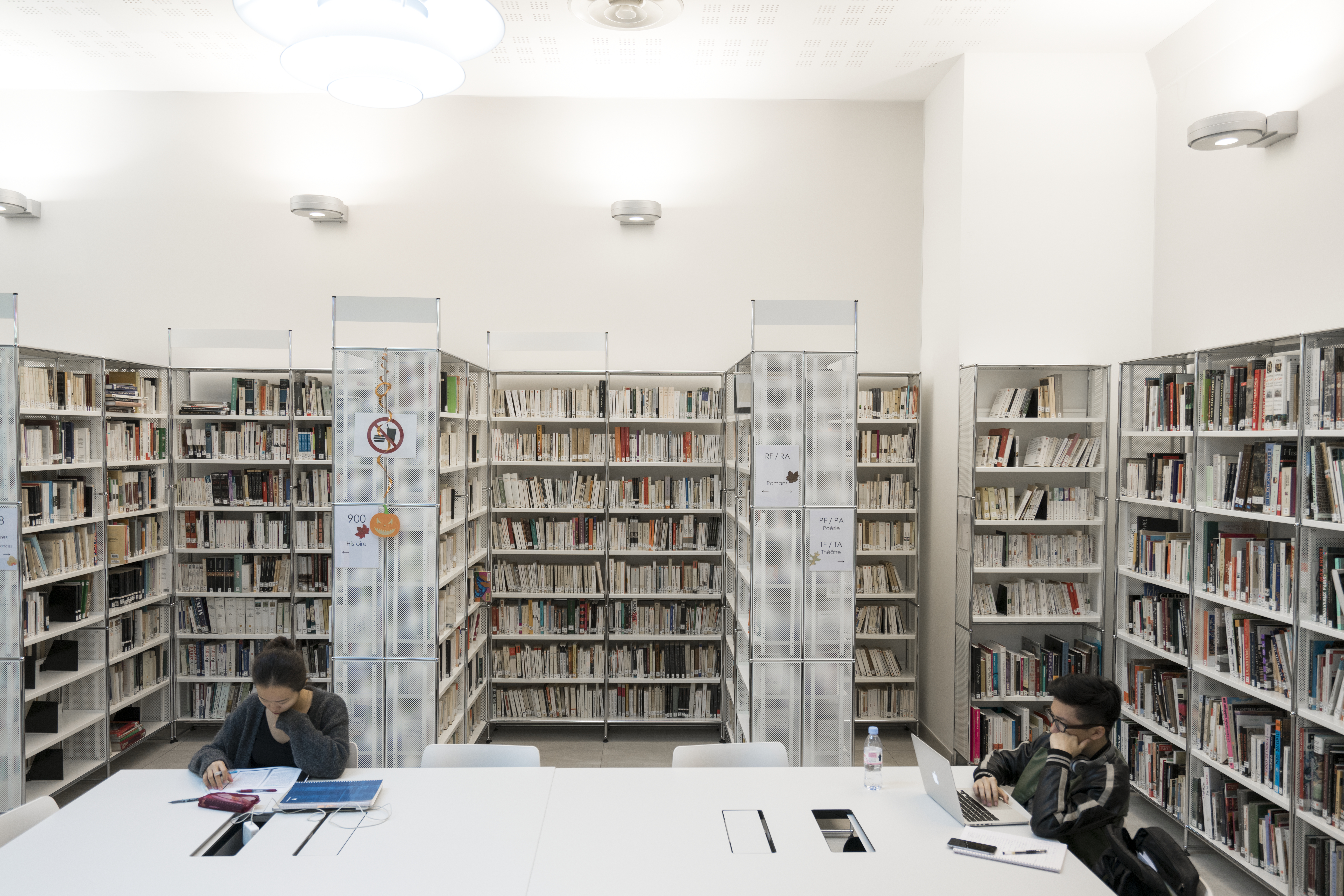 Two students studying in a library surrounded by bookshelves.